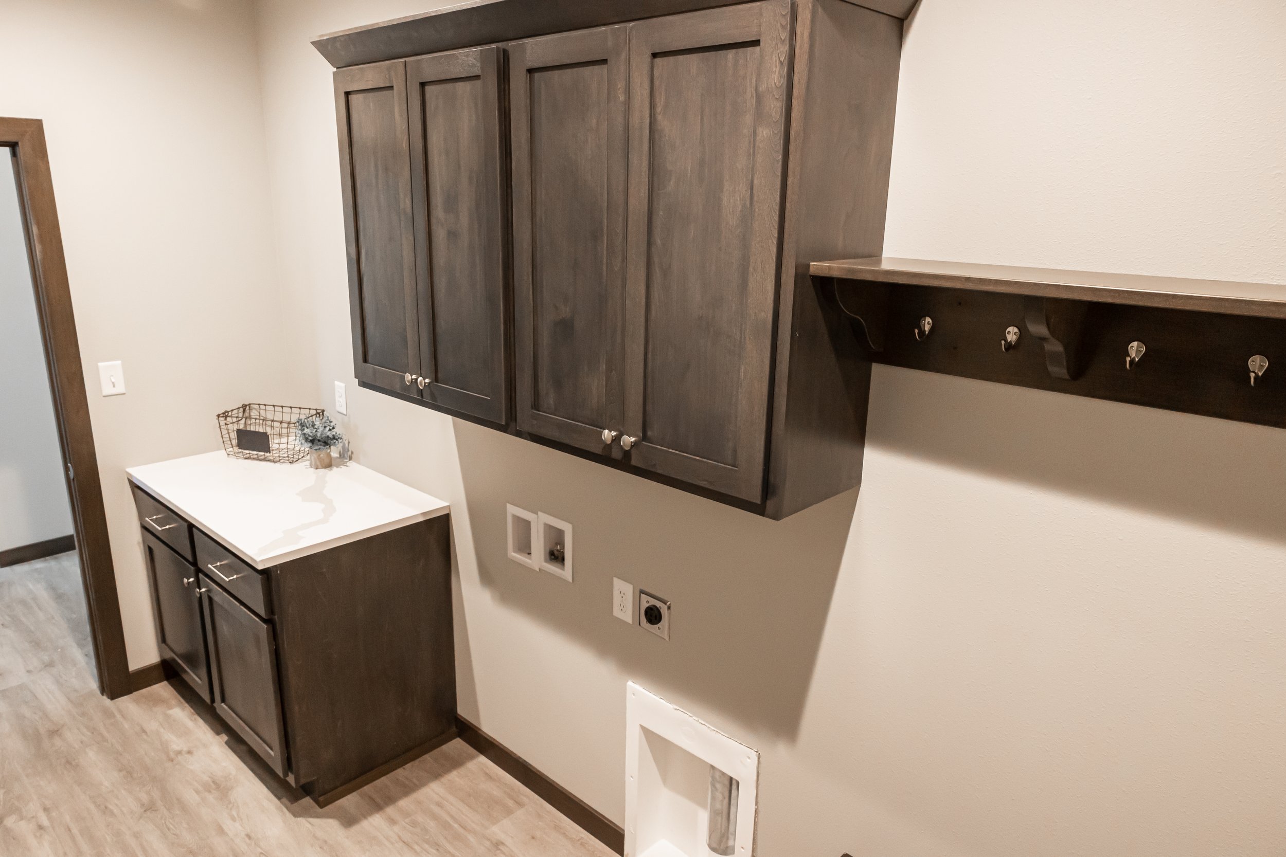 Laundry room with wooden cabinets, a countertop, wall hooks, and plumbing outlets for appliances.