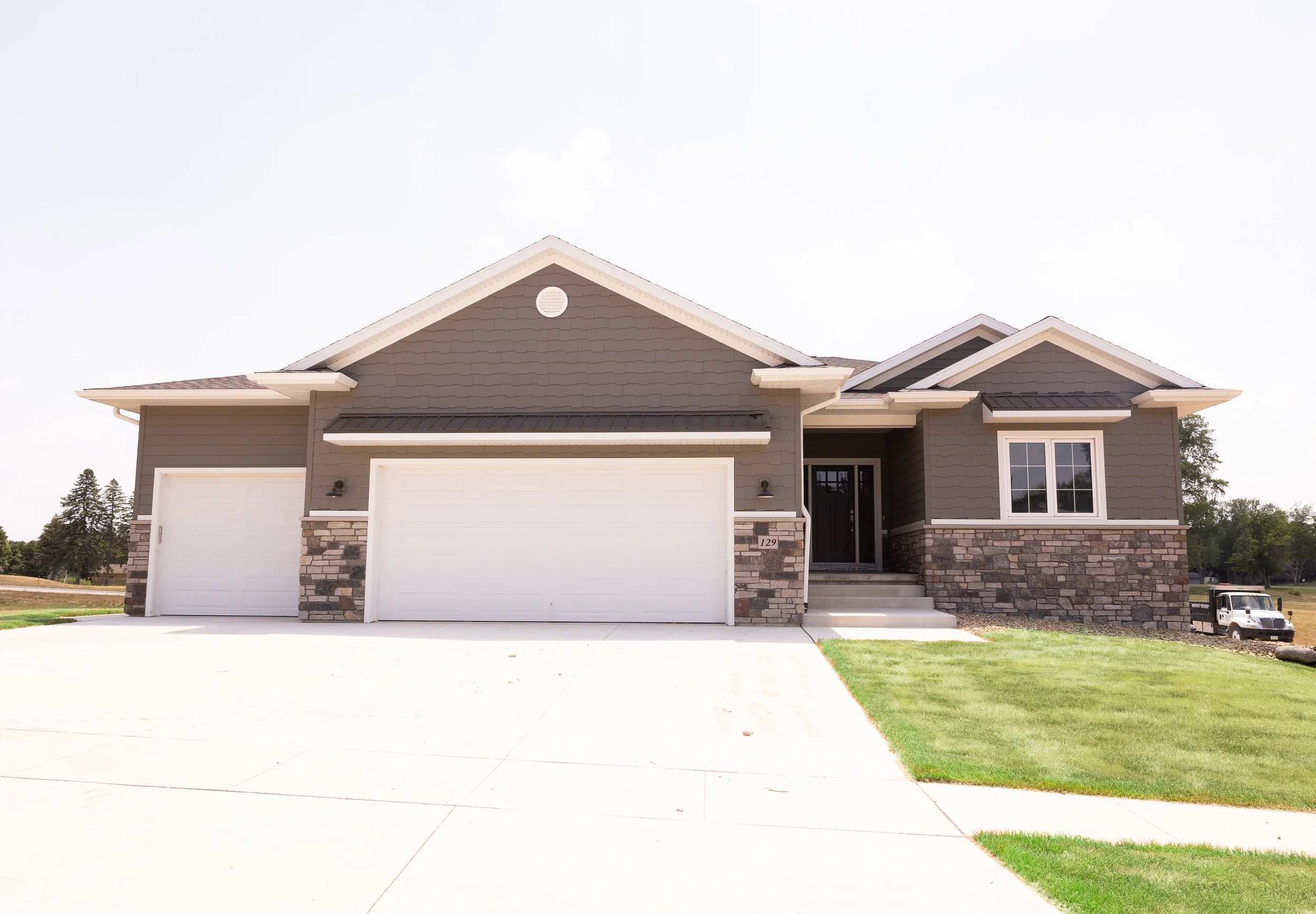 Modern single-story house with attached garage, gray siding, stone accents, and manicured lawn.