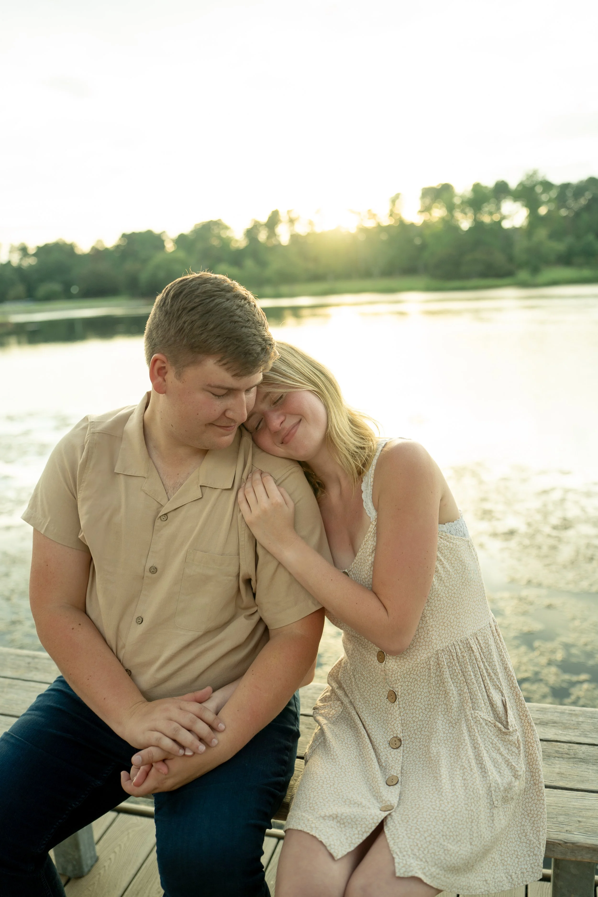 woman laying on man's shoulder on a bench with a sunset over a lake in the background