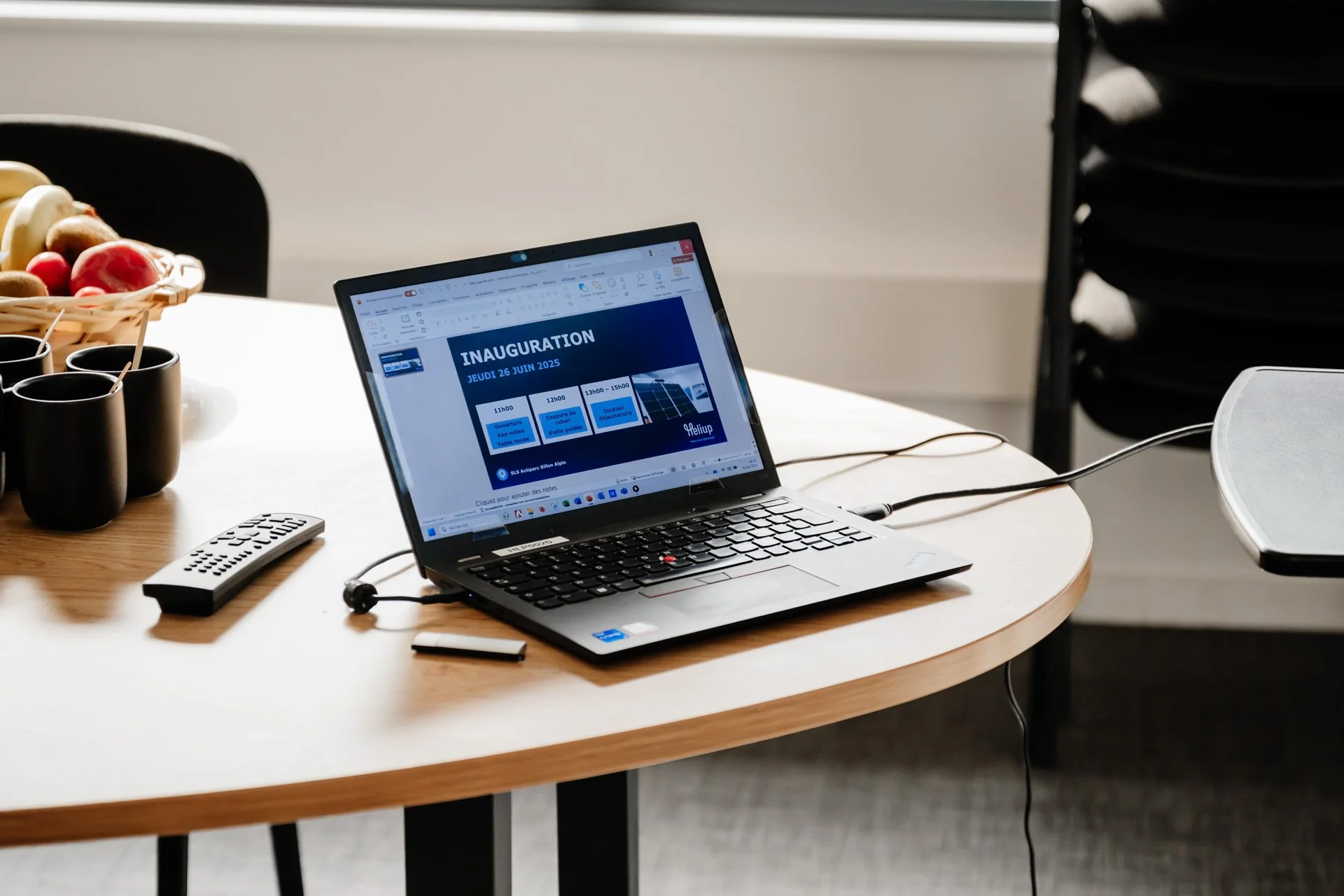 Ordinateur portable affichant le programme de l’inauguration du 26 juin 2025 d’Heliup, posé sur une table de réunion avec boissons et documents.