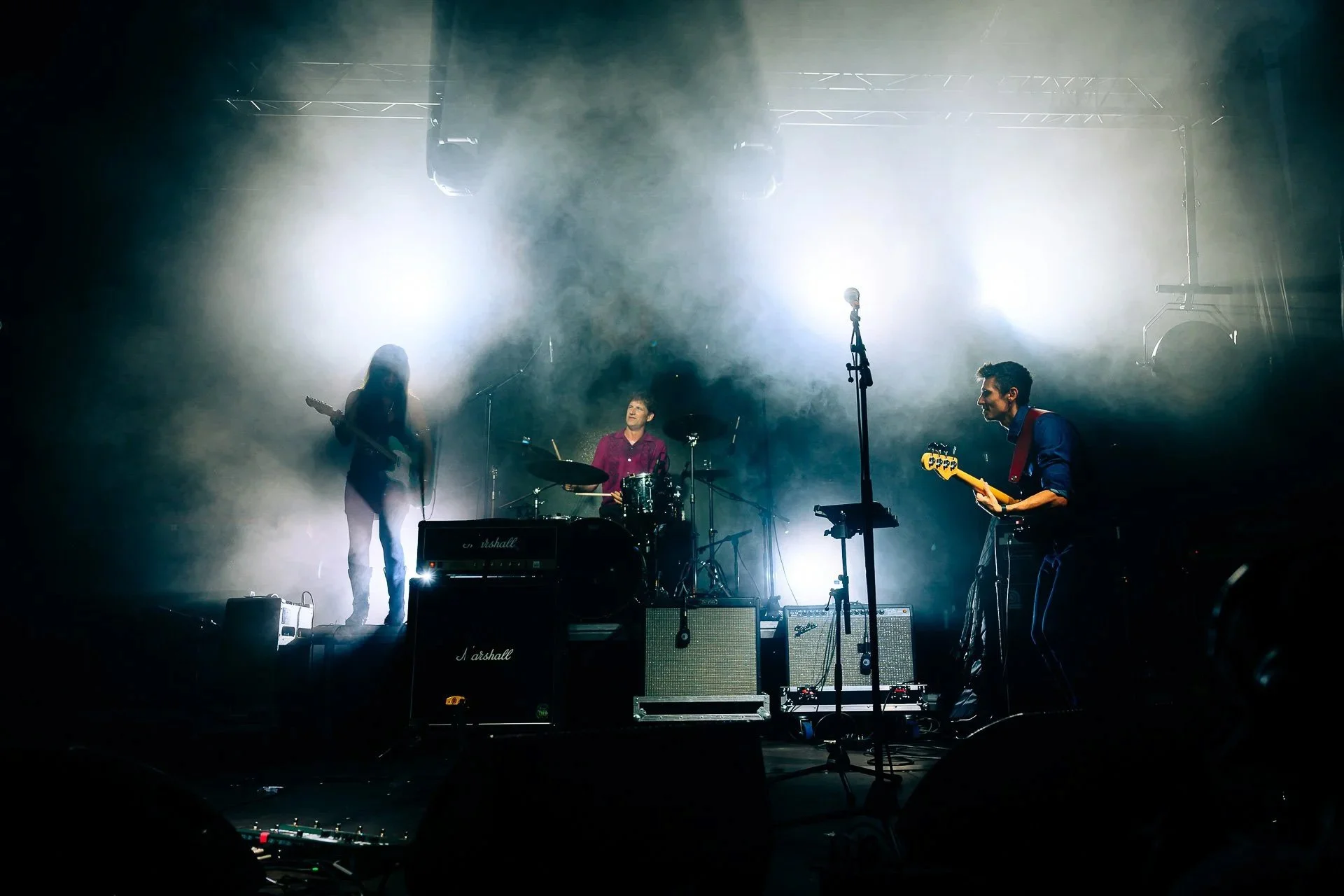Groupe de musique en pleine performance sur scène, fumée et éclairages créant une atmosphère immersive.
