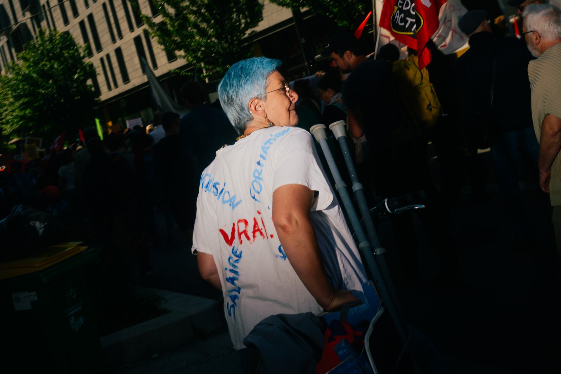 Femme de dos avec des béquilles et un t-shirt revendicatif pendant la mobilisation pour l’éducation publique à Grenoble – reportage photo documentaire.