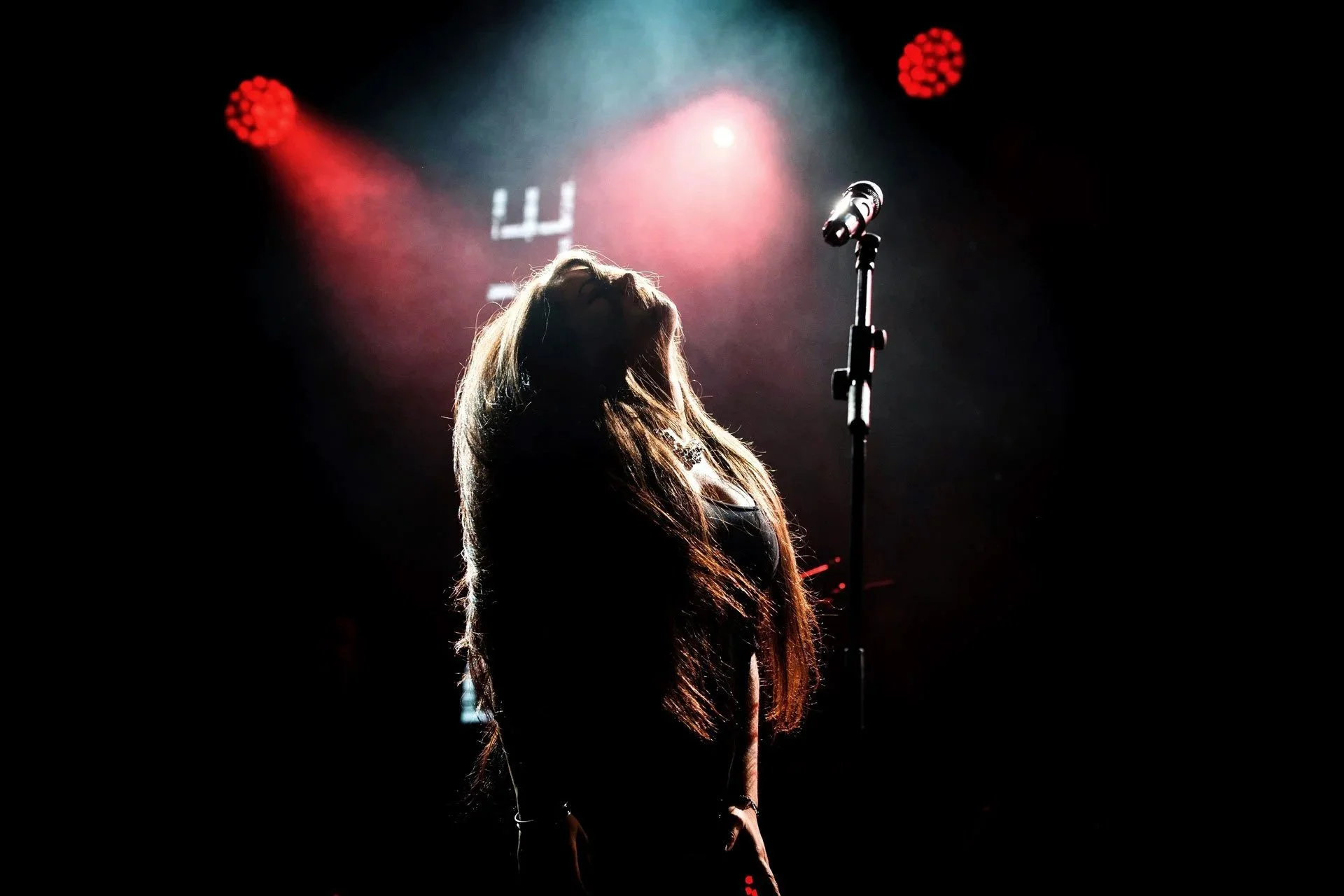 Artiste en contre-jour sur scène pendant un concert, ambiance sombre et jeu de lumières spectaculaires.