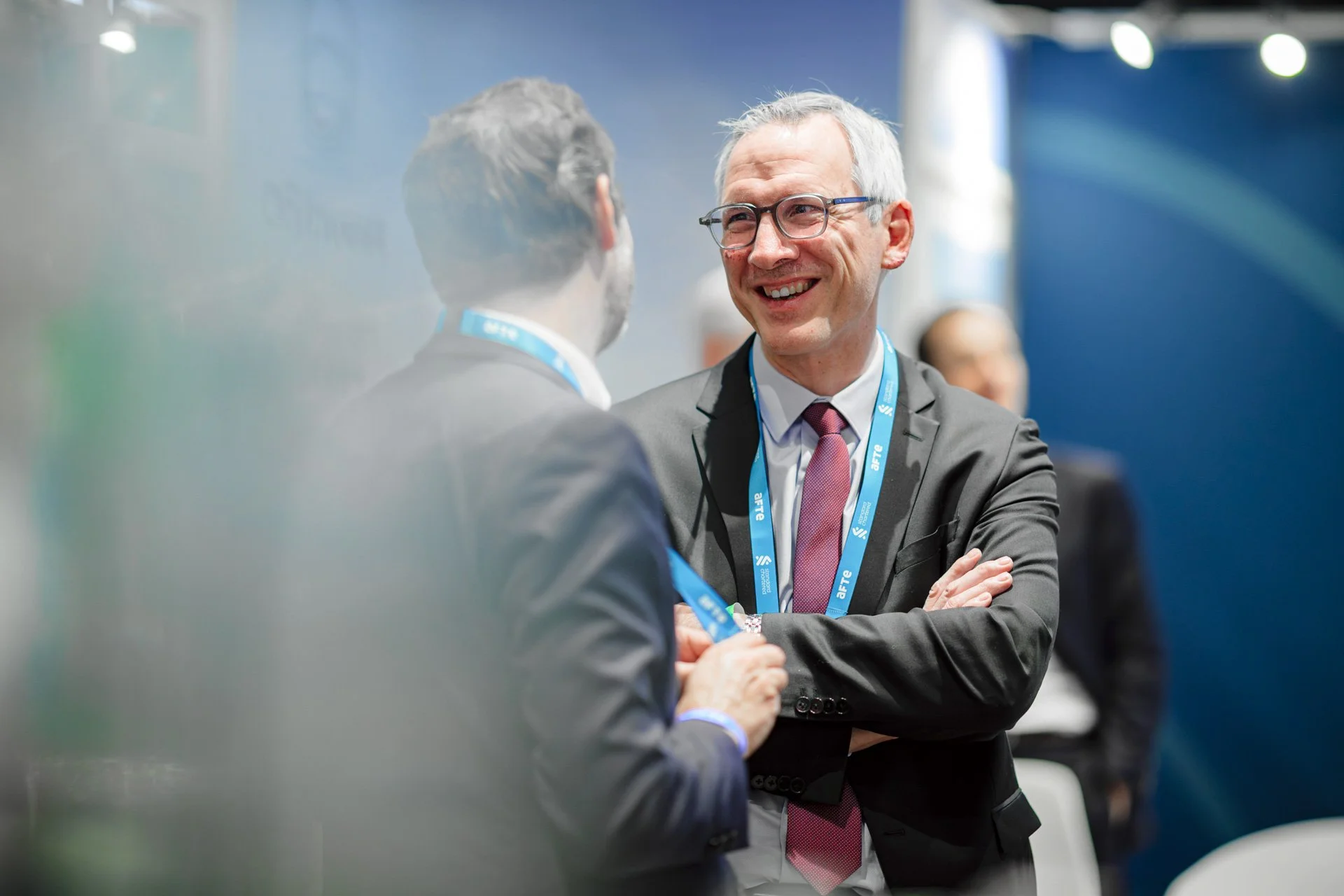 Échange chaleureux entre deux participants dans l’espace exposant des Journées de l’AFTE 2025, capté en mode portrait professionnel.