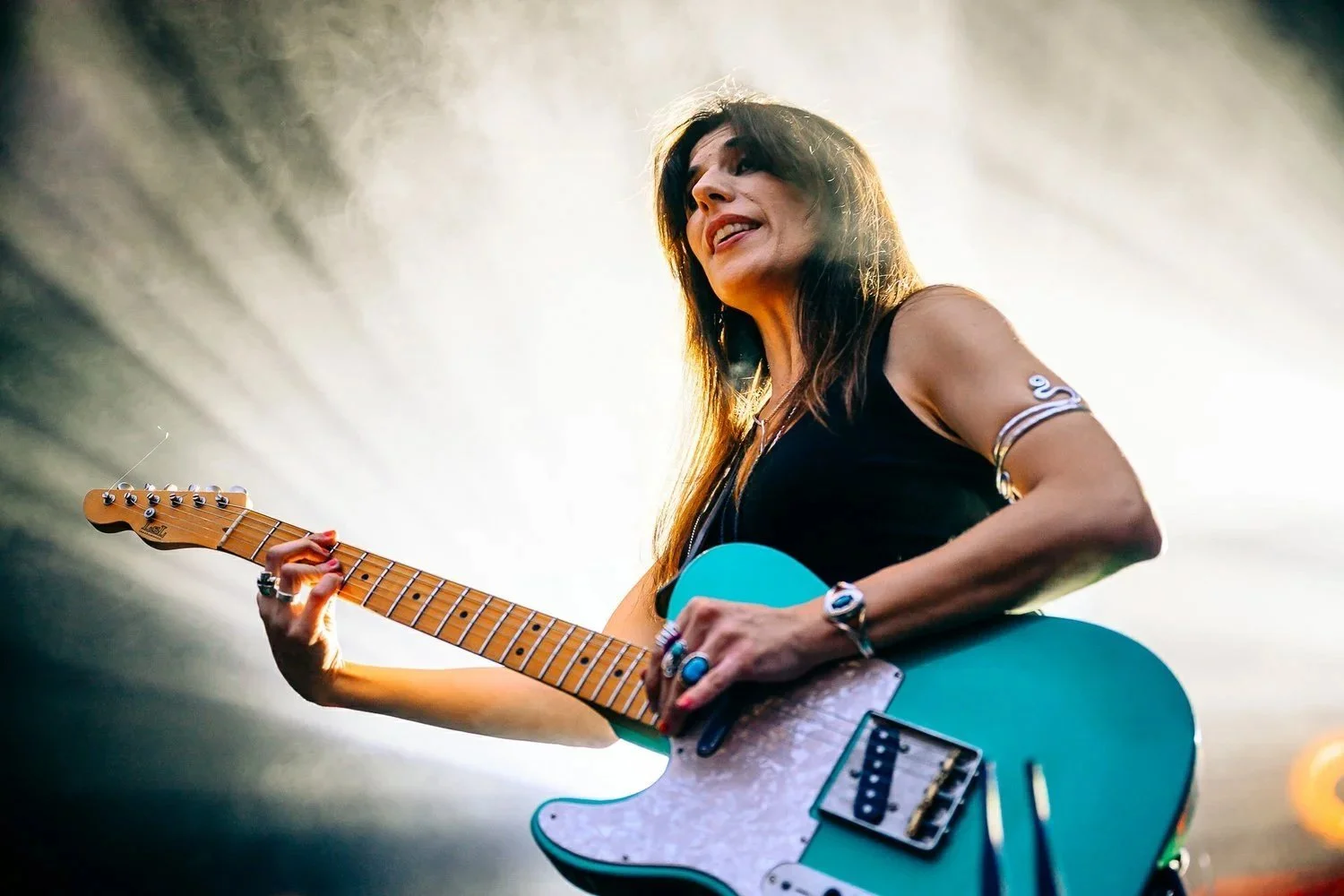 Guitariste sur scène pendant un concert, jeu instrumental et lumière puissante photographiés en contre-plongée.