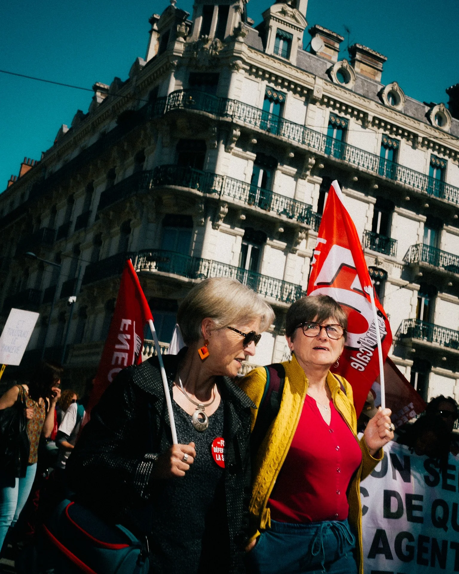 Deux femmes défilant avec des drapeaux rouges et pancartes lors de la manifestation des enseignants à Grenoble.