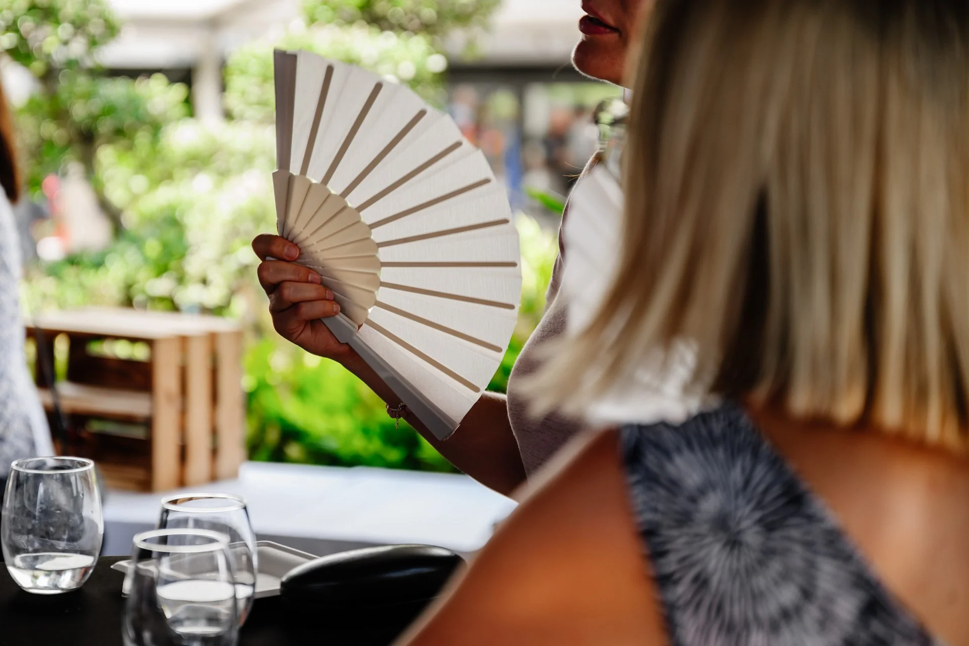 Invitée se rafraîchissant avec un éventail lors du cocktail en extérieur.