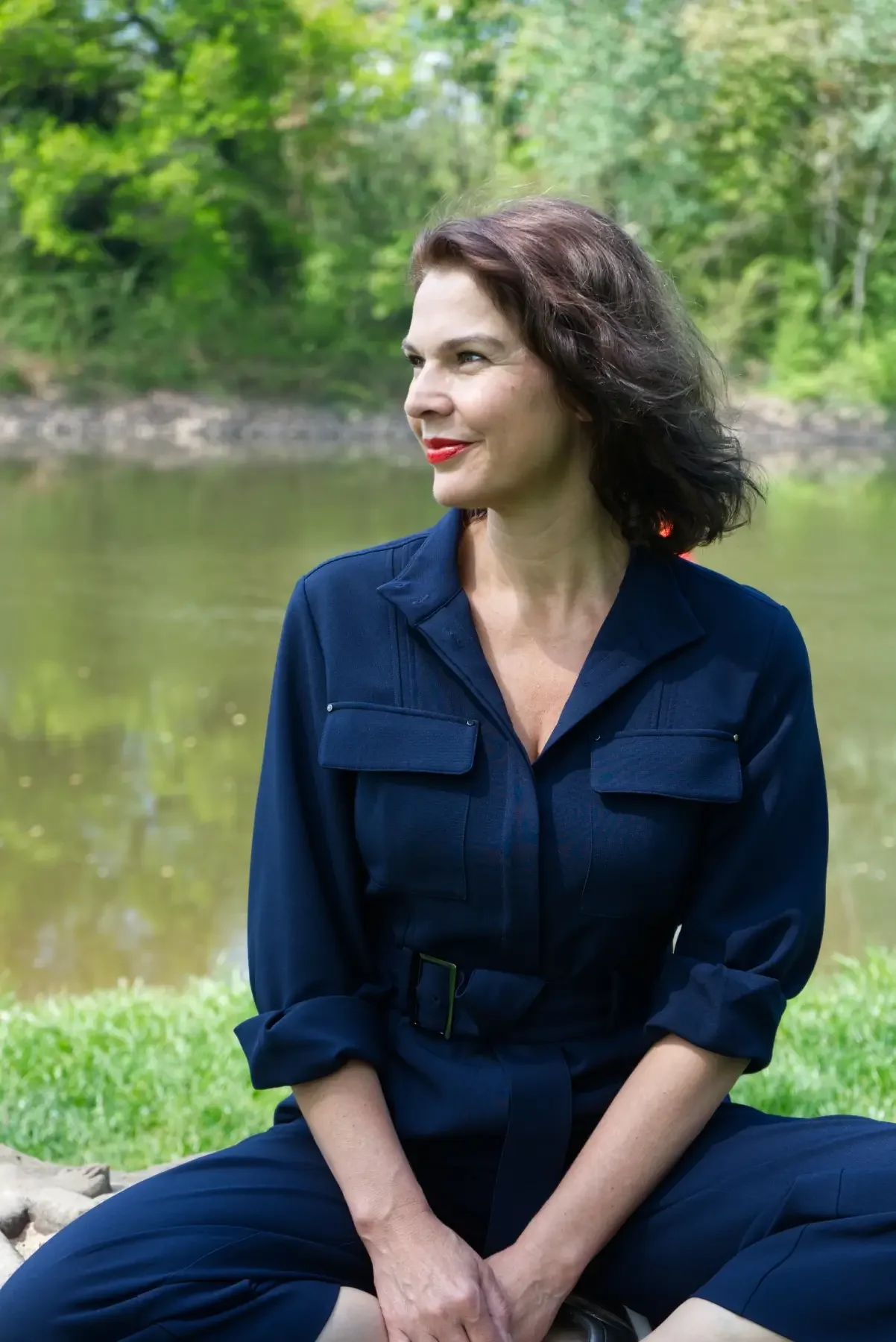 Alexandra Poser sitzt am Ufer der Saale in Halle und blickt lächelnd zur Seite – Porträt der Mentorin und systemischen Coachin.