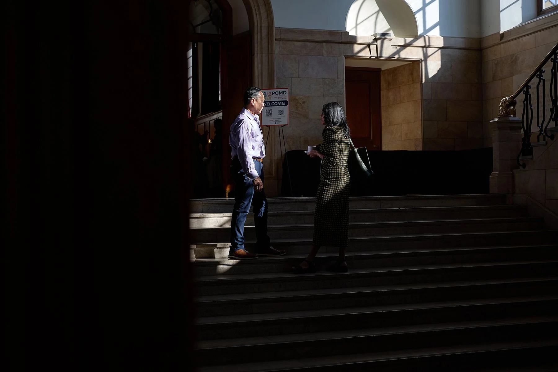 A man and woman talking on the stairs inside a building, with sunlight coming through windows.