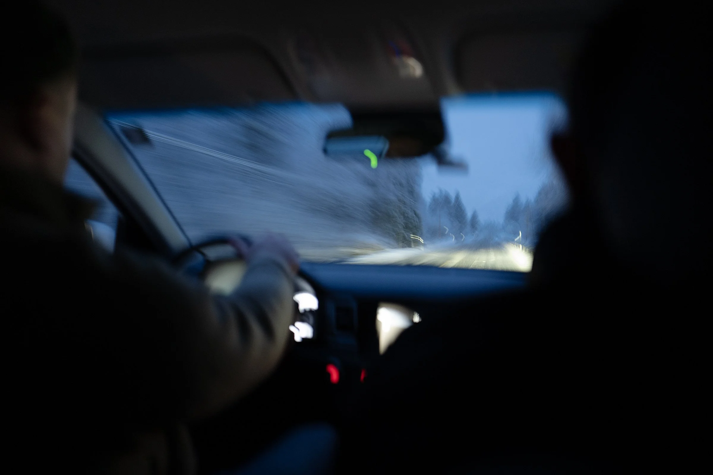 Interior view of a car traveling on a snowy road at night, with two passengers in the front seats
