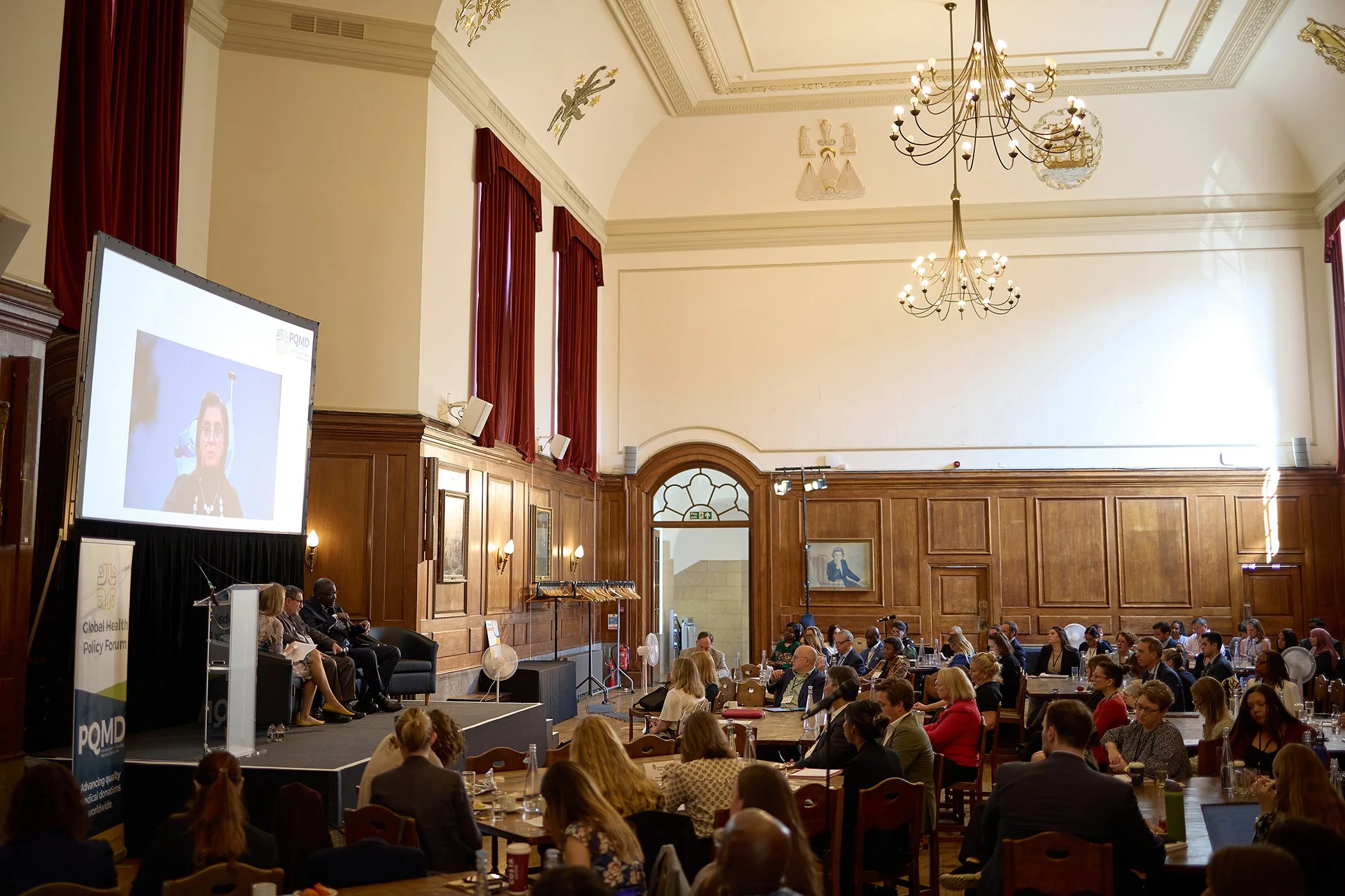 Wide-angle event photography of the World Health Summit in the Great Hall at Goodenough College, London, capturing the scale and atmosphere of the IHP and PQMD forum.