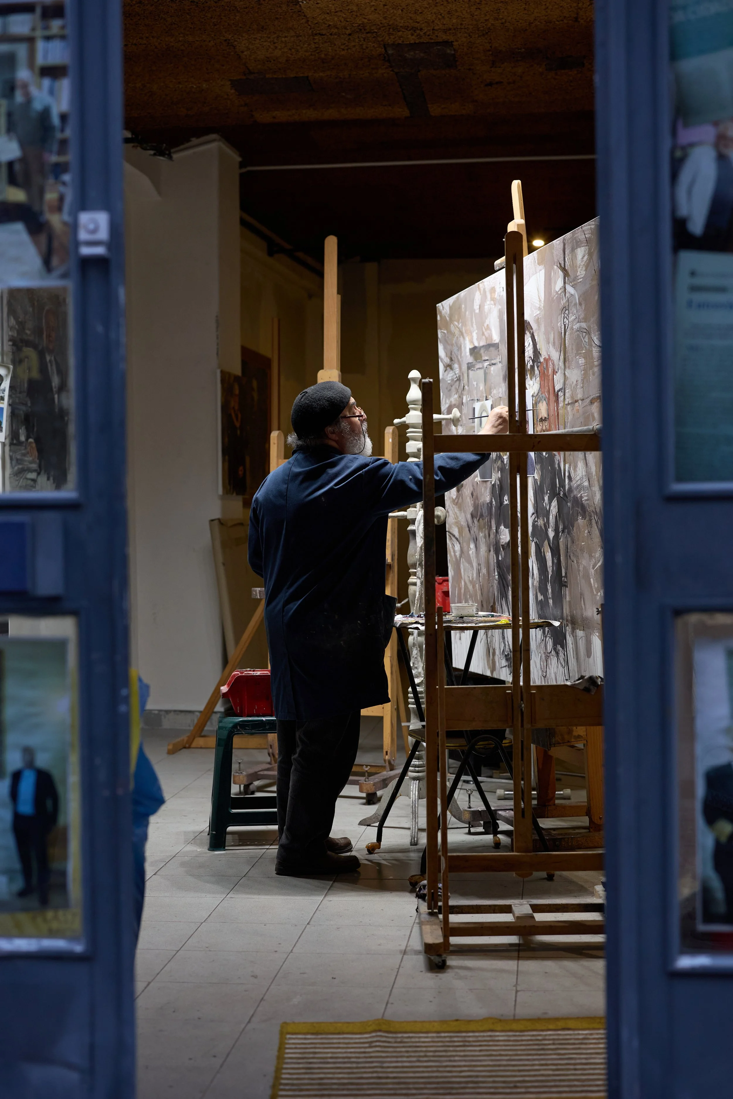 Documentary‑style image of artist Antonio Bessa working between canvases