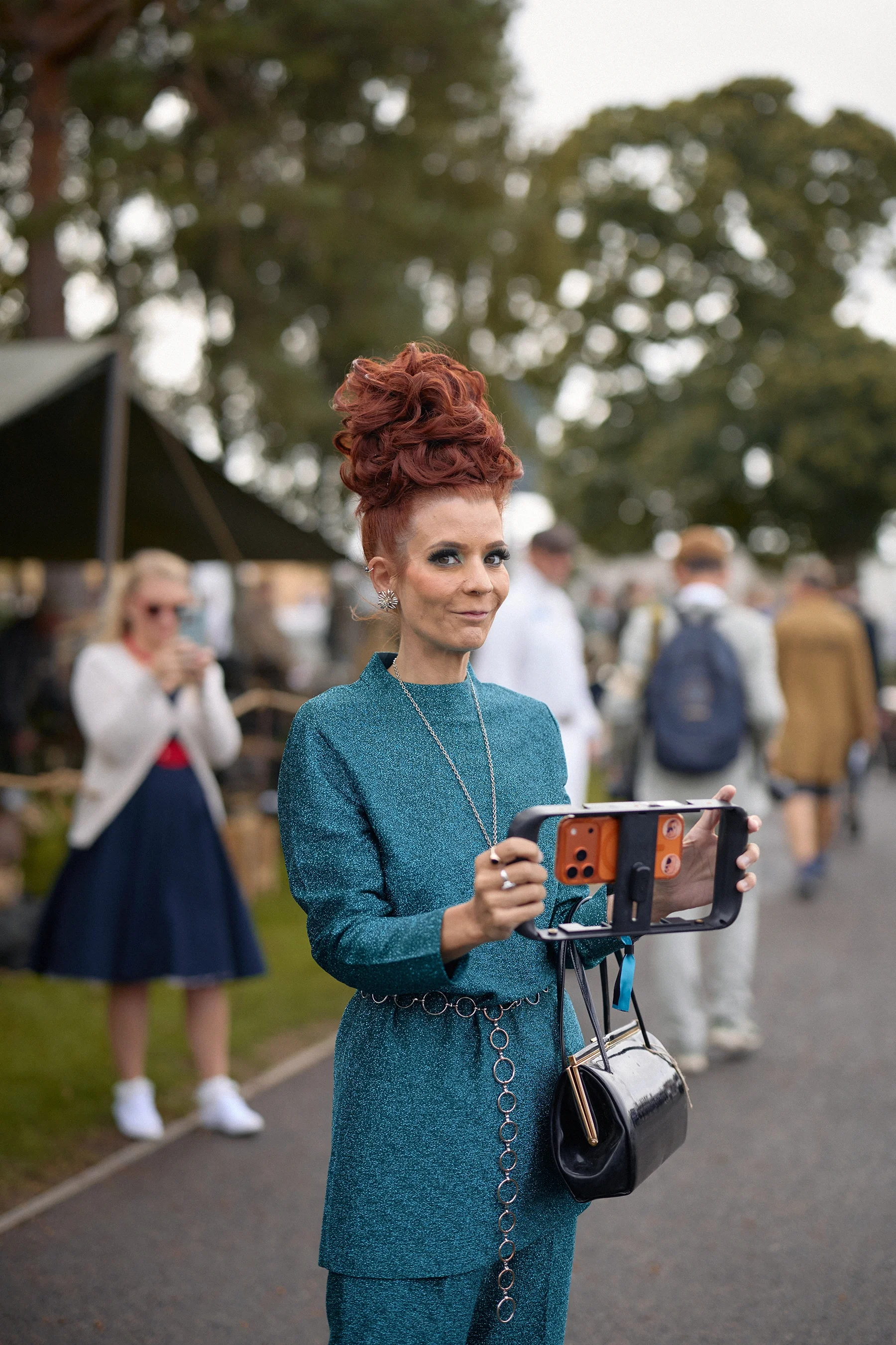 Woman in vintage fashion holding an iPhone 15 Pro with a video grip at Goodwood Revival 2026