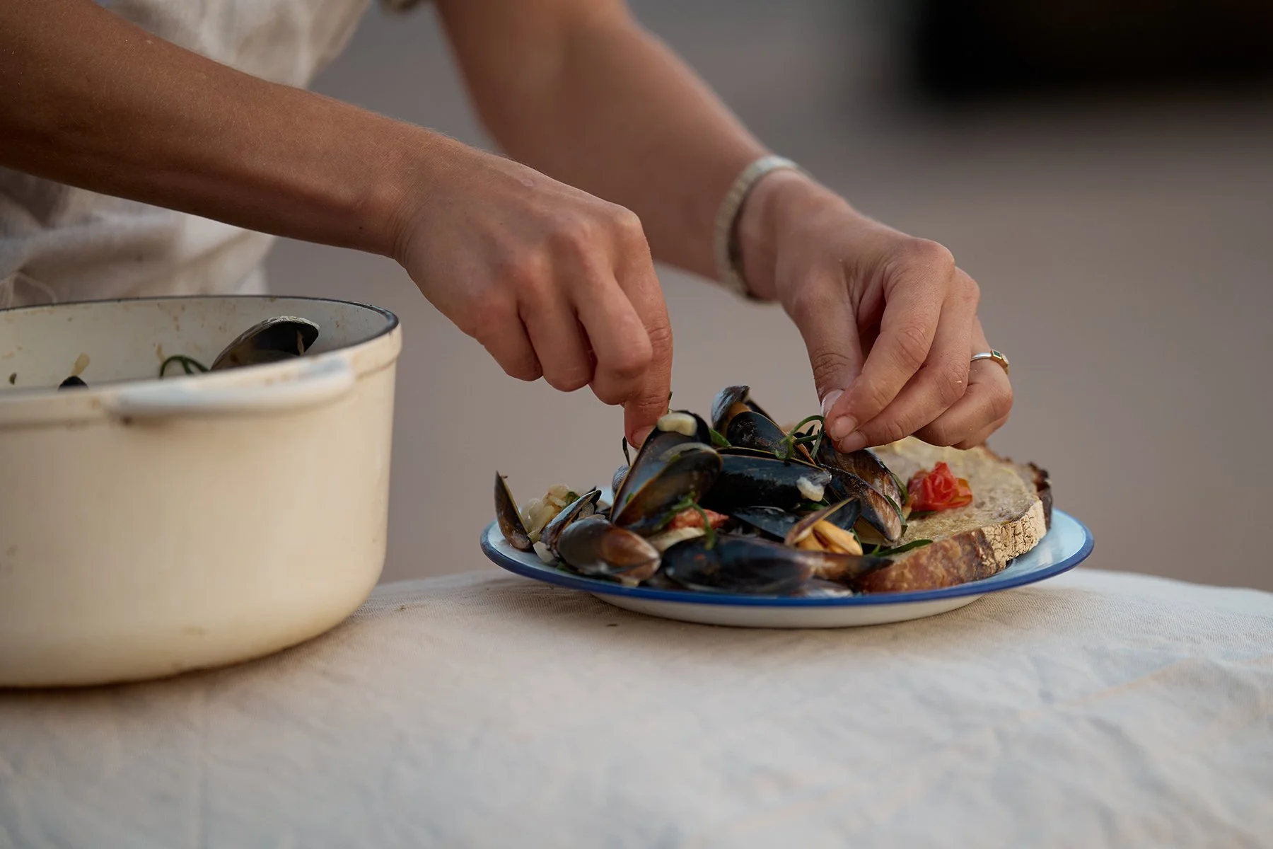 Person preparing mussels and bread for a meal on a table.