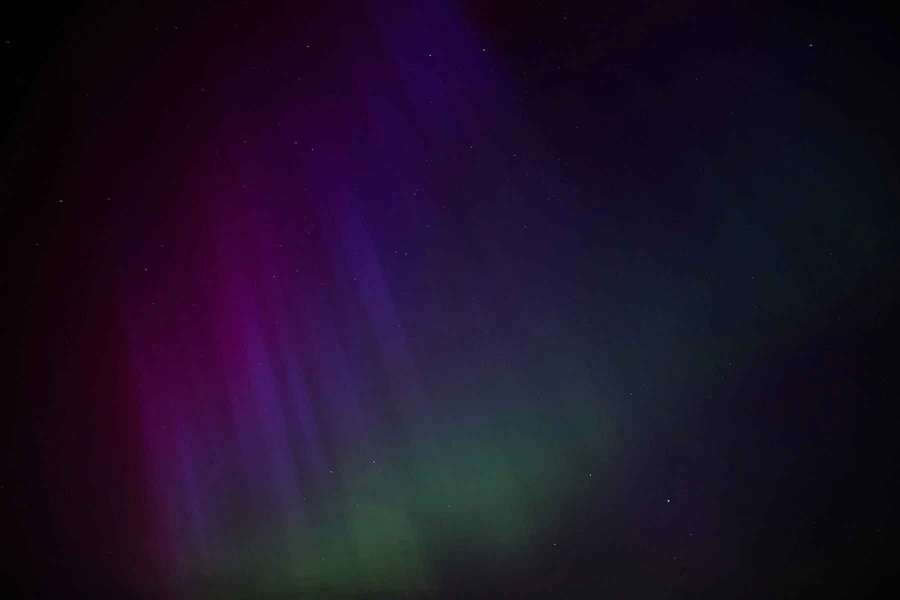 Night sky with colorful aurora borealis in shades of purple, green, and blue, with faint stars visible.