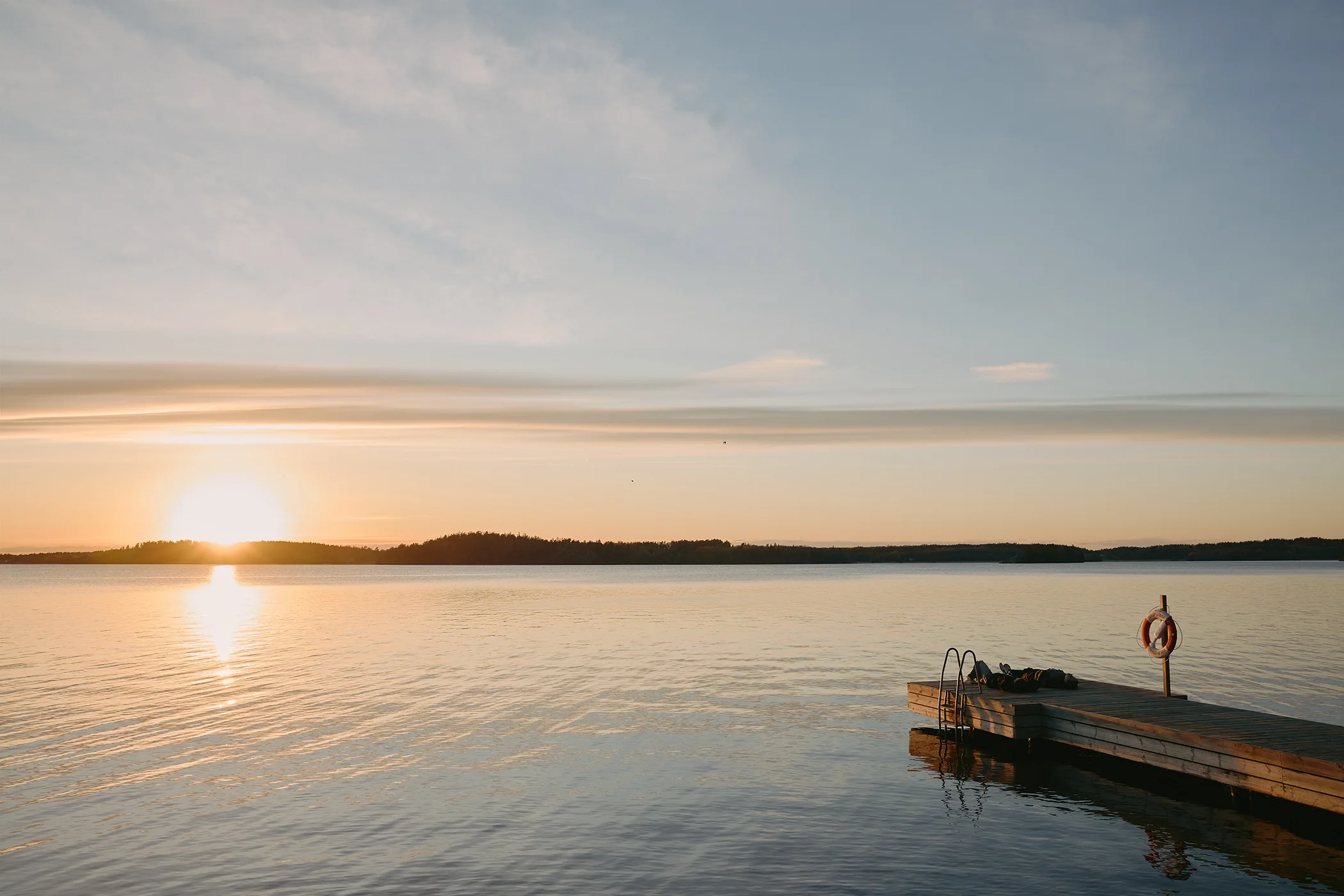 Wide angle photograph of two figures in a Scandinavian coastal sunset scene in Sweden