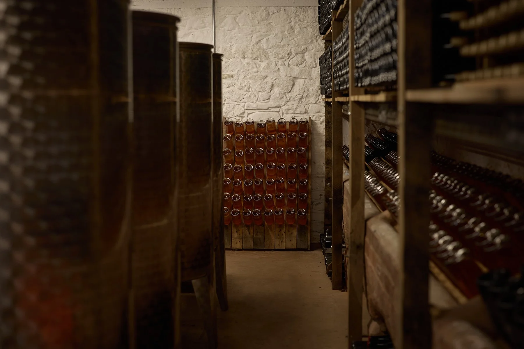 A cellar or wine storage room with shelves of wine bottles and a pallet of unopened wine bottles in the back.