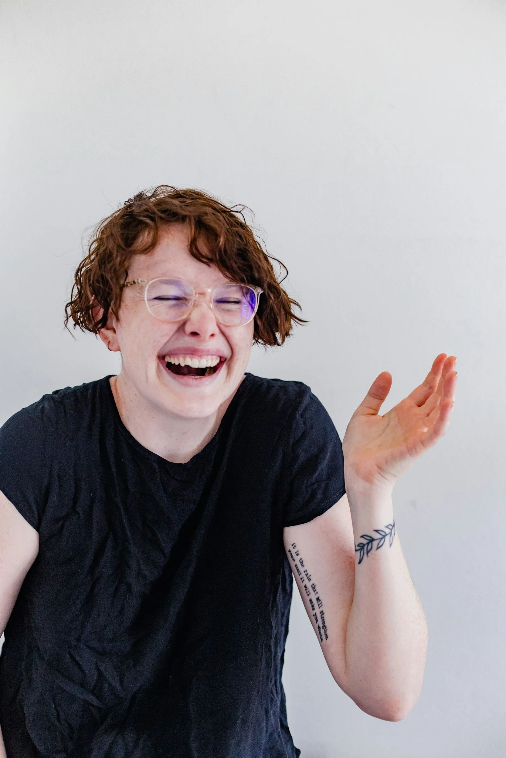 Queer polyamorous person with short red hair and glasses, laughing