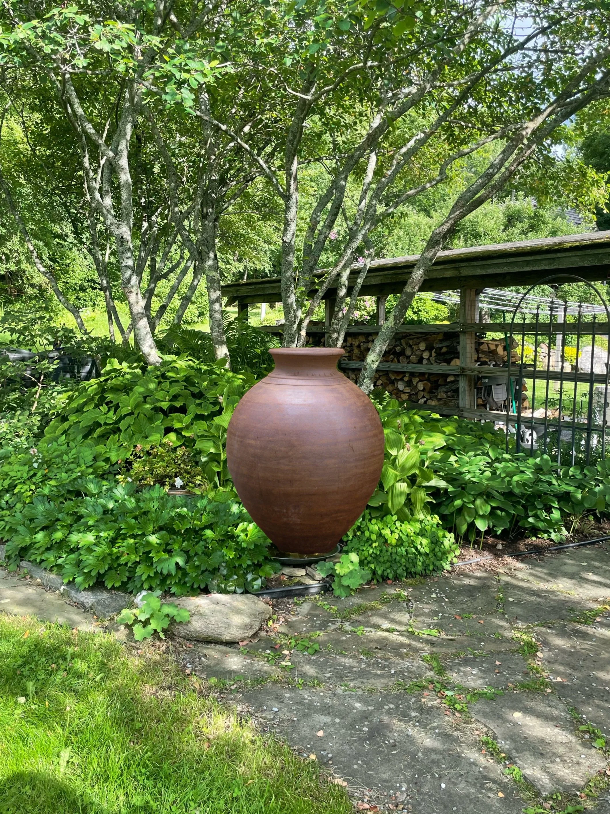 Large terracotta pot placed among lush greenery beside stone path in landscaped garden