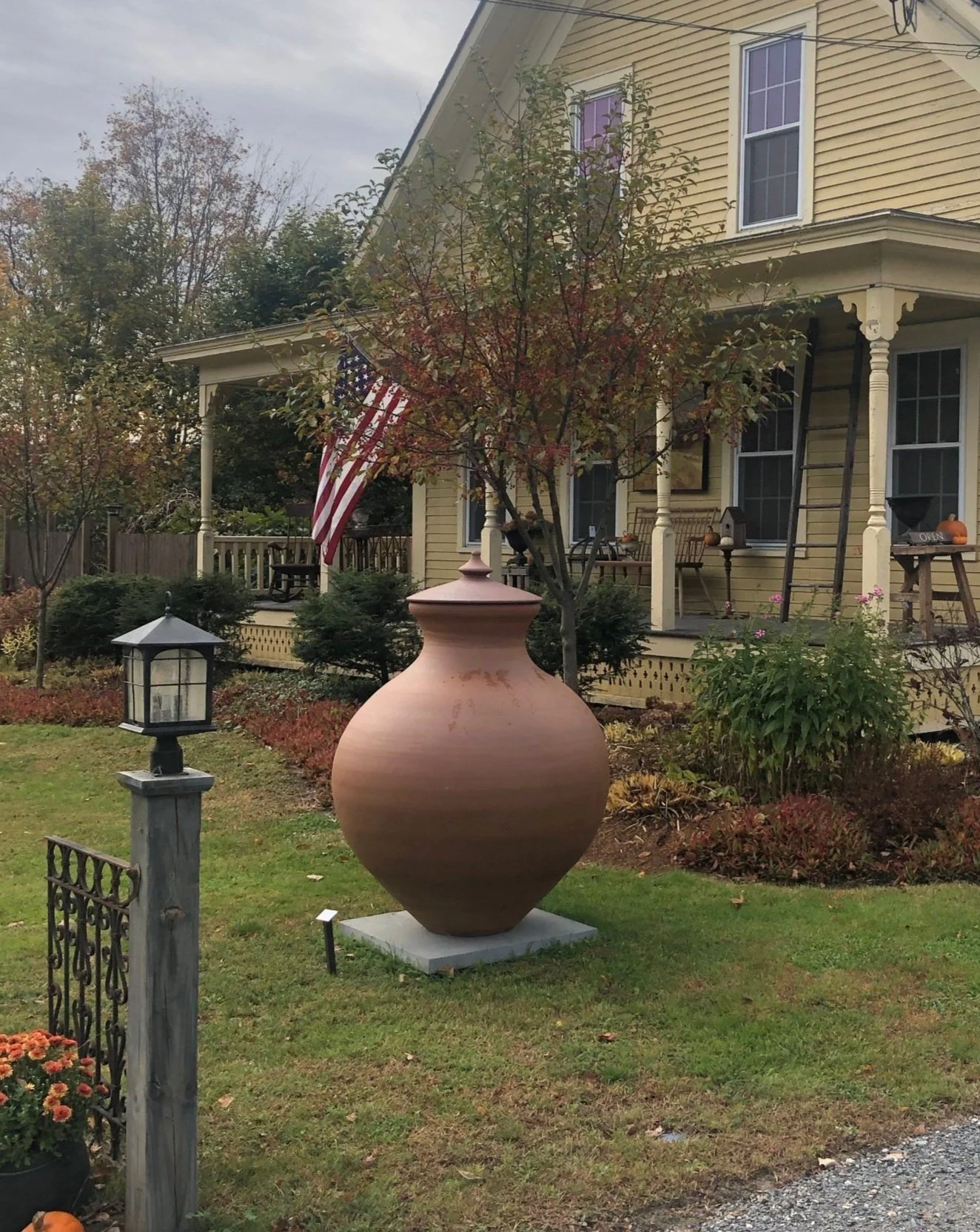 Tall terracotta pot displayed in front of yellow house with American flag and garden lamps