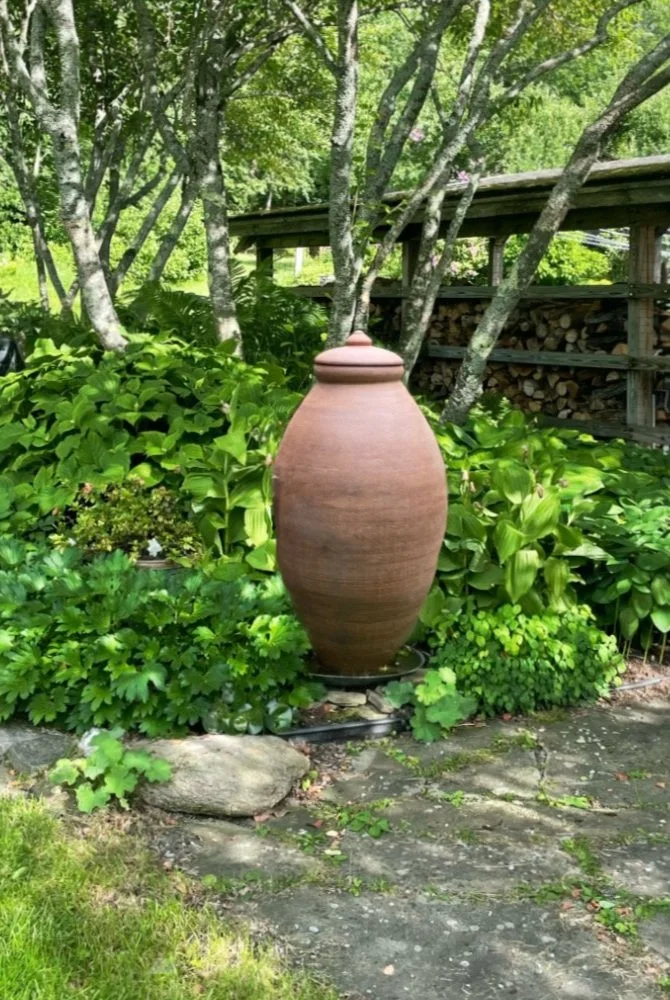 Clay vessel with lid positioned on stone surface with foliage in background