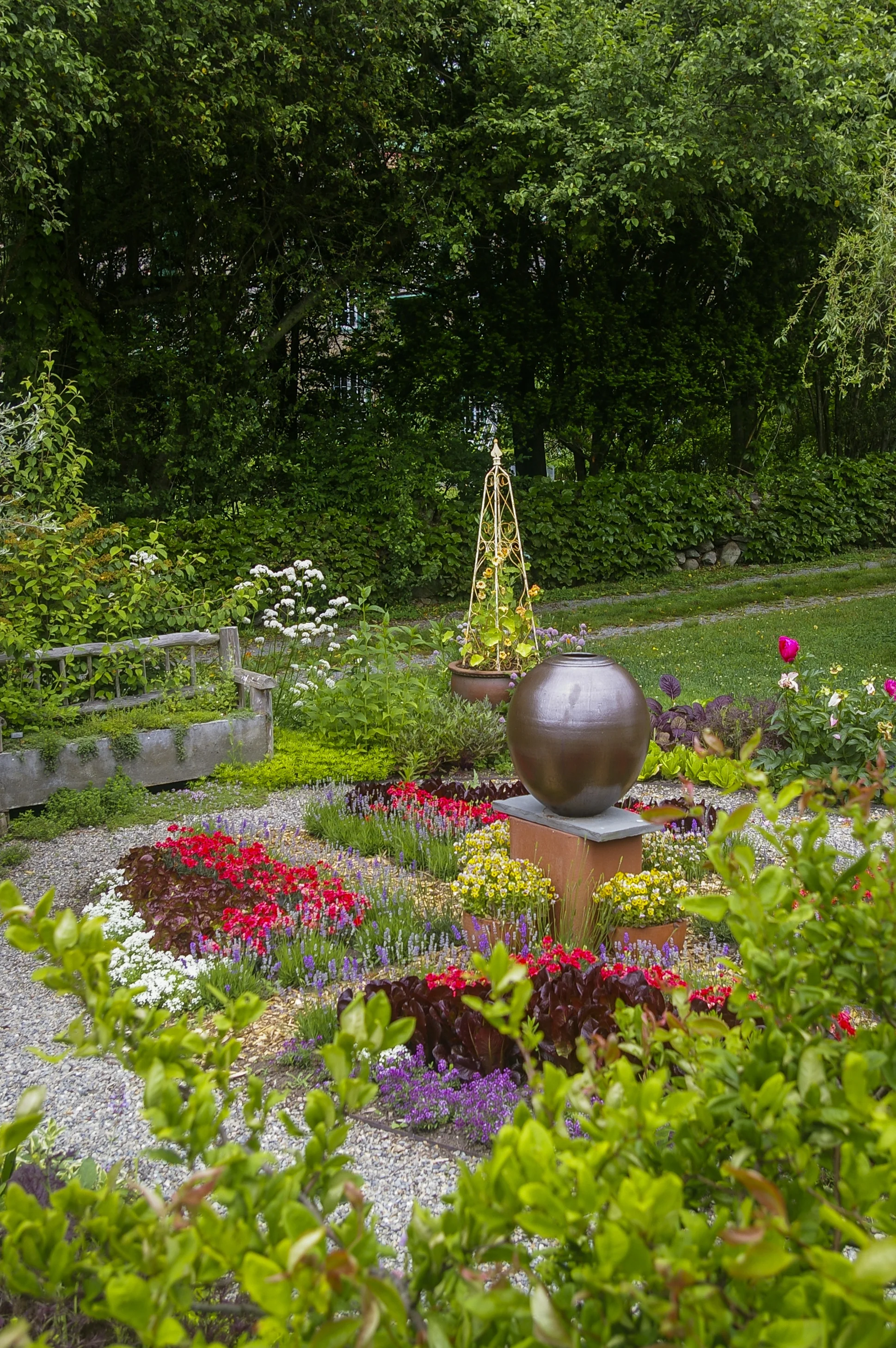Large clay vessel positioned among trees and mulch in landscaped garden