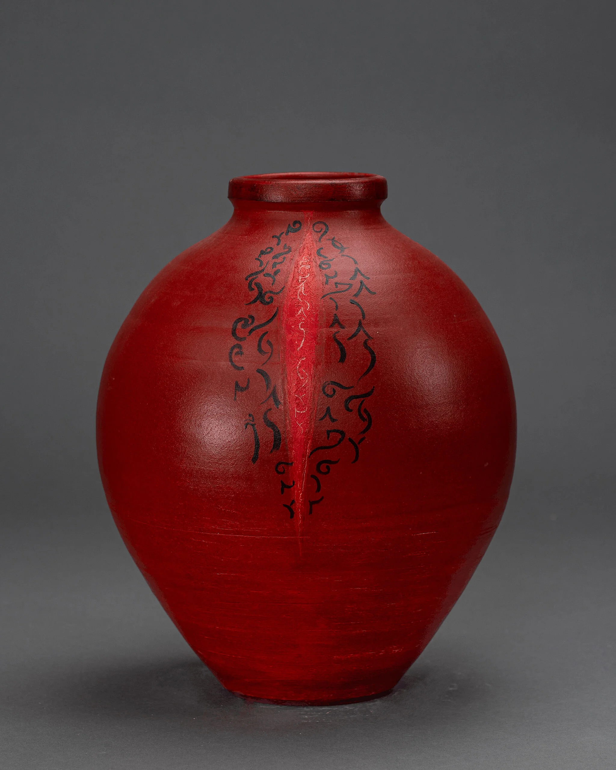 Tall red pottery vase decorated with subtle black markings