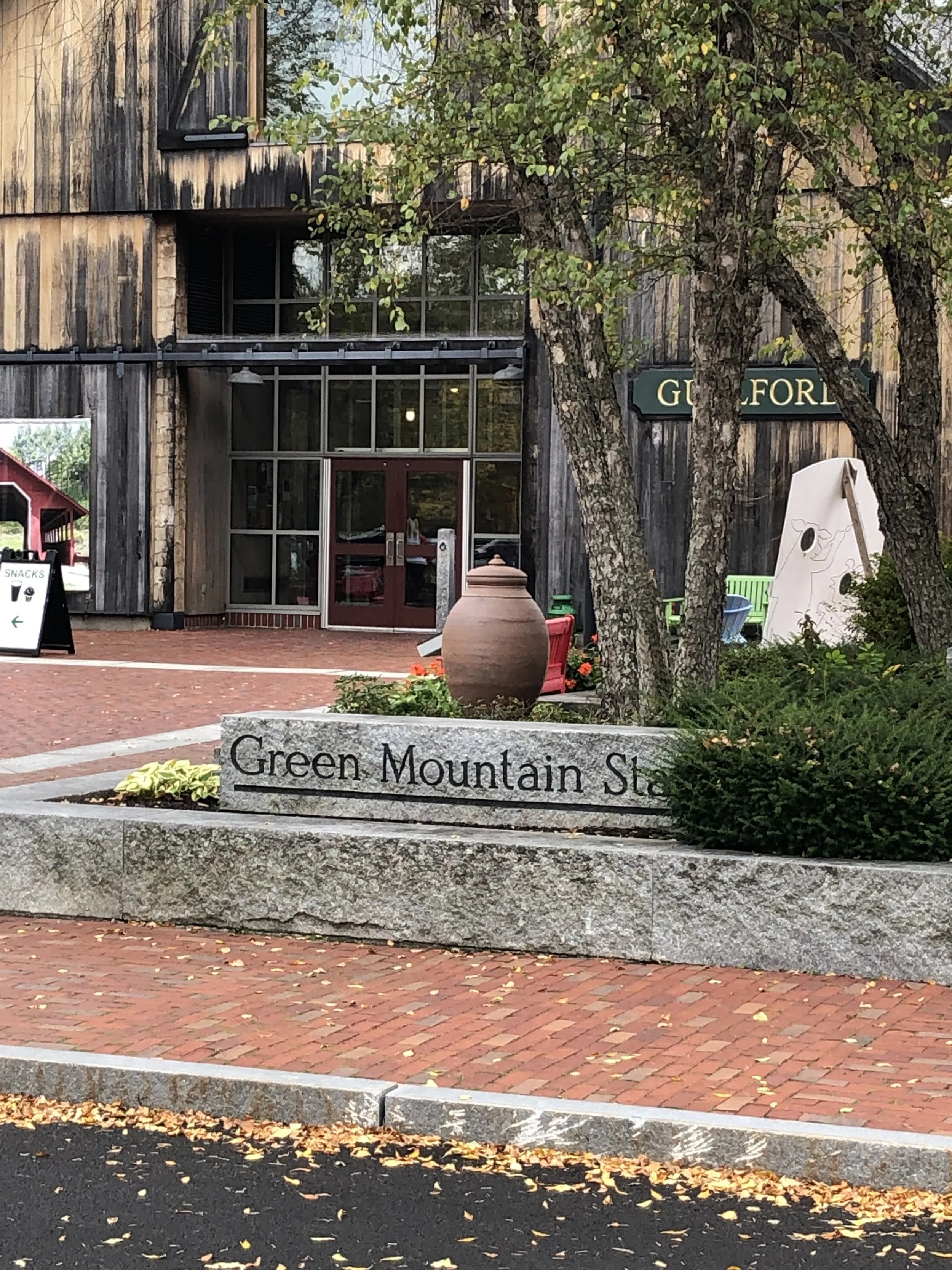 Rustic building with Green Mountain State stone sign, clay pot, shrubs, and brick-paved visitor area.