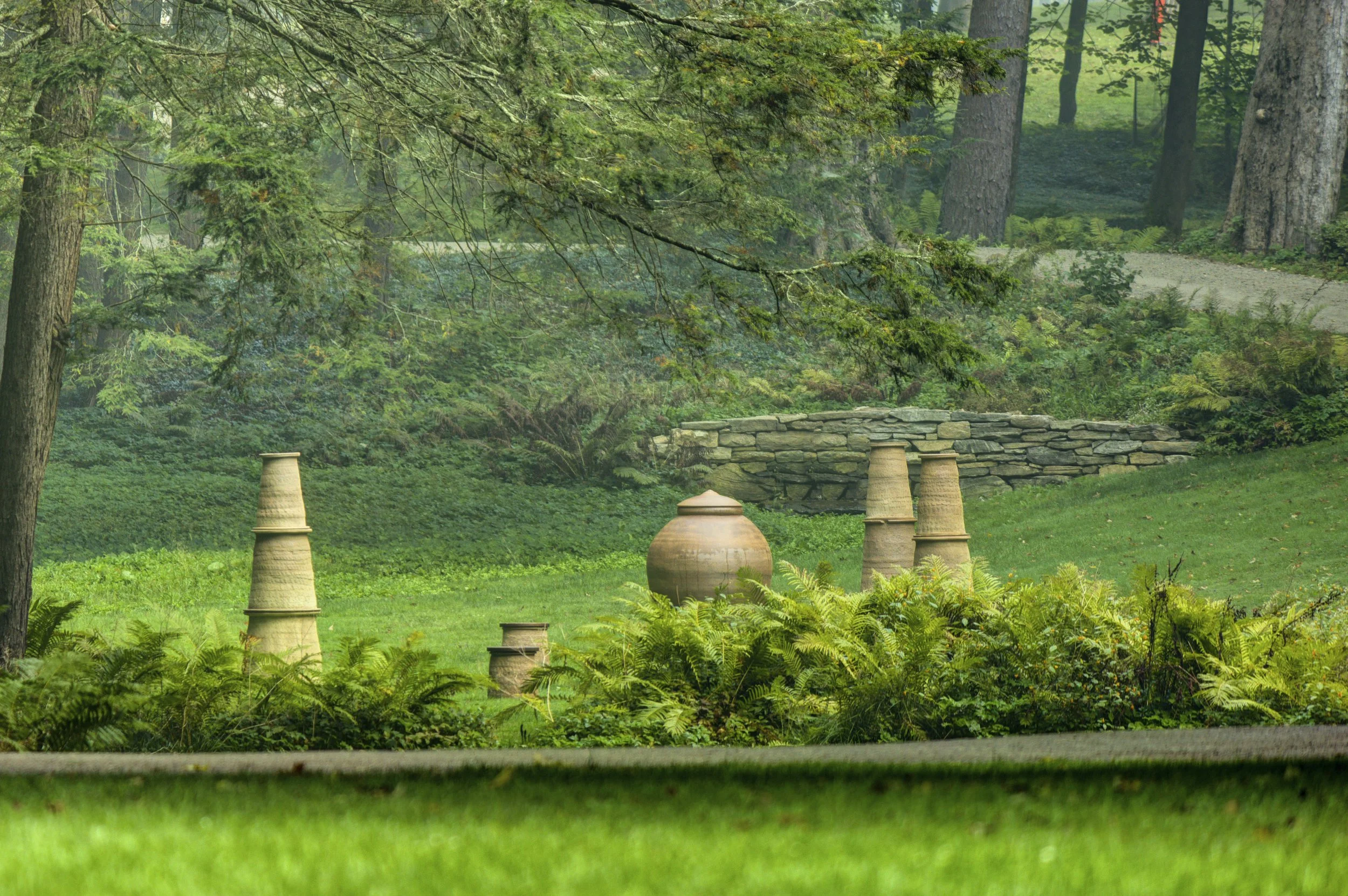 Large clay urn-shaped sculpture placed on grassy lawn during outdoor art exhibition 