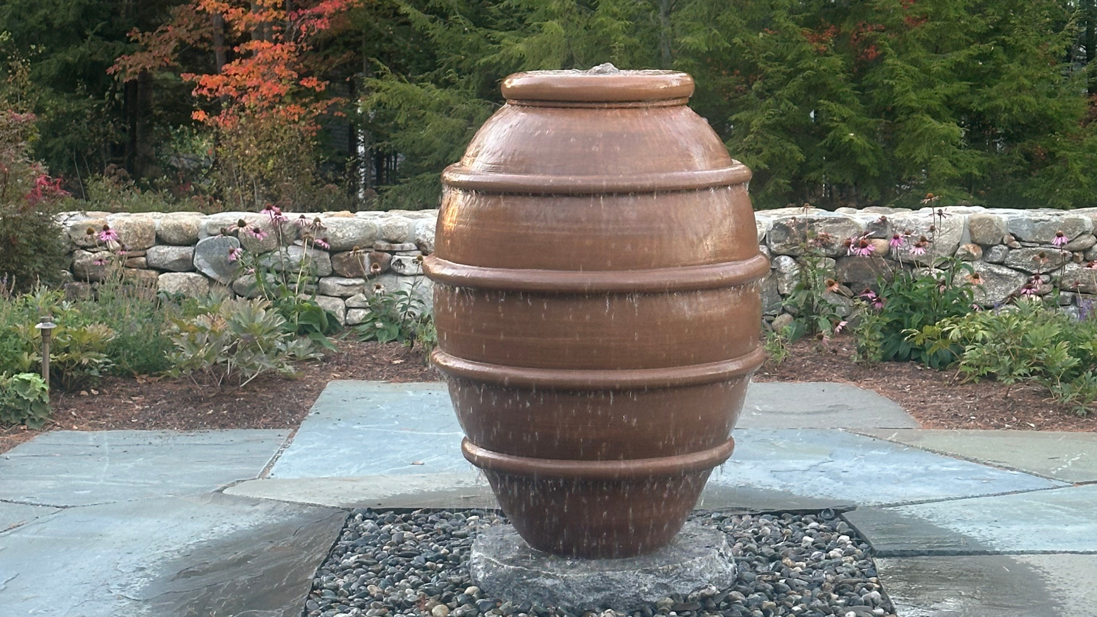 Large round ceramic vessel with lid displayed outdoors among trees and greenery