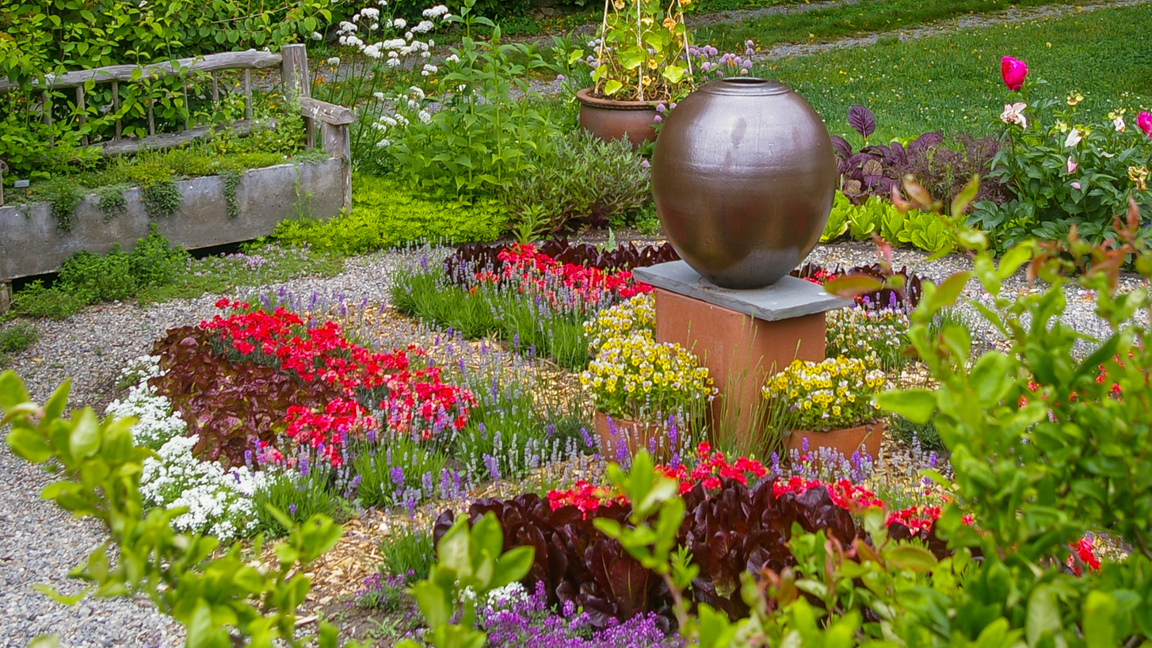 Handcrafted ceramic vessel placed near a tree and metal bench in garden setting
