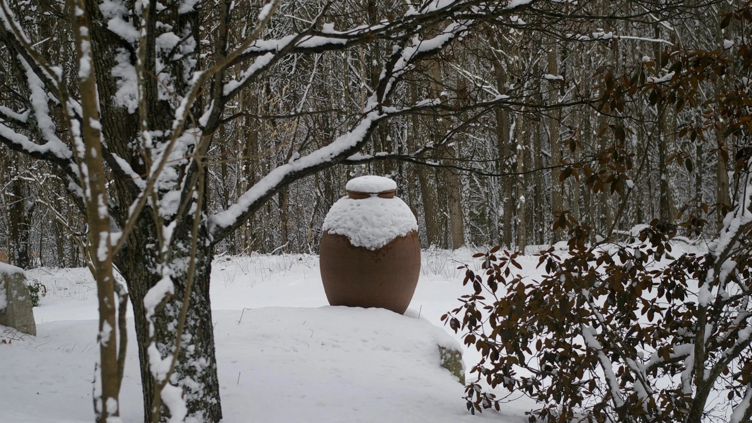 Large pottery jar outdoors in snowy winter landscape.
