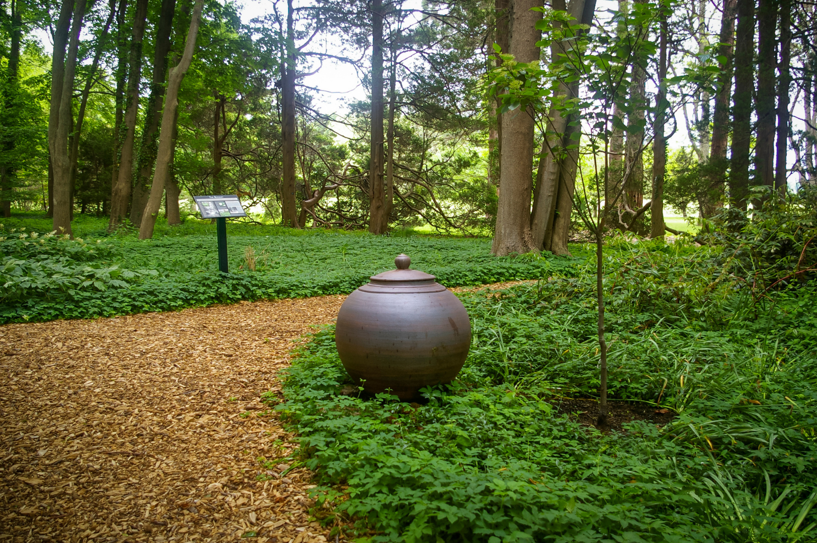 Rounded clay urn displayed in garden with trees and stone features