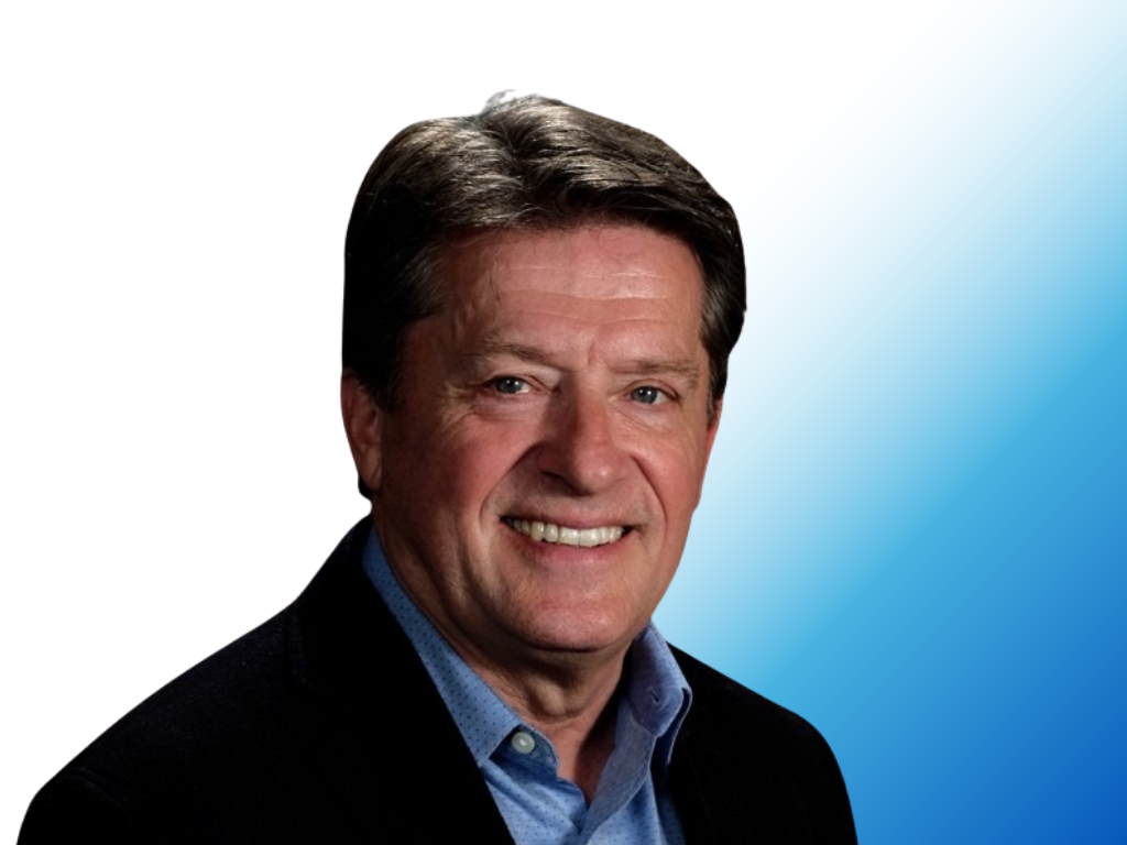 A headshot of a man with dark brown hair, smiling, wearing a dark blazer over a light blue shirt, with a gradient blue background.