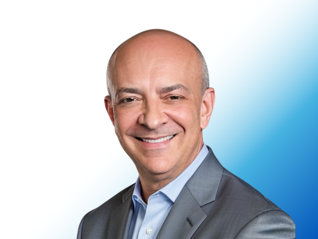 Smiling middle-aged man in a gray suit and light blue shirt against a blue and white background.