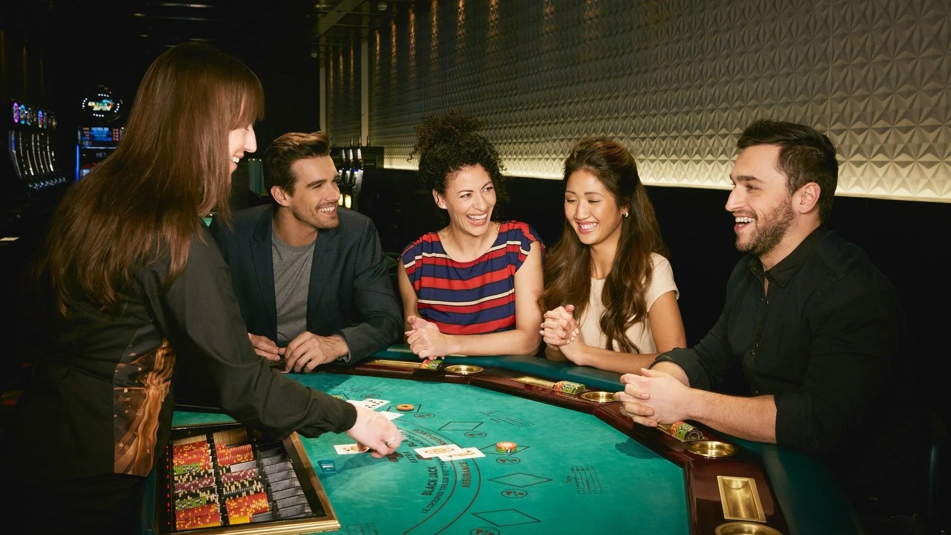 A group of five diverse people, three women and two men, are playing blackjack at a casino table, smiling and enjoying their game.