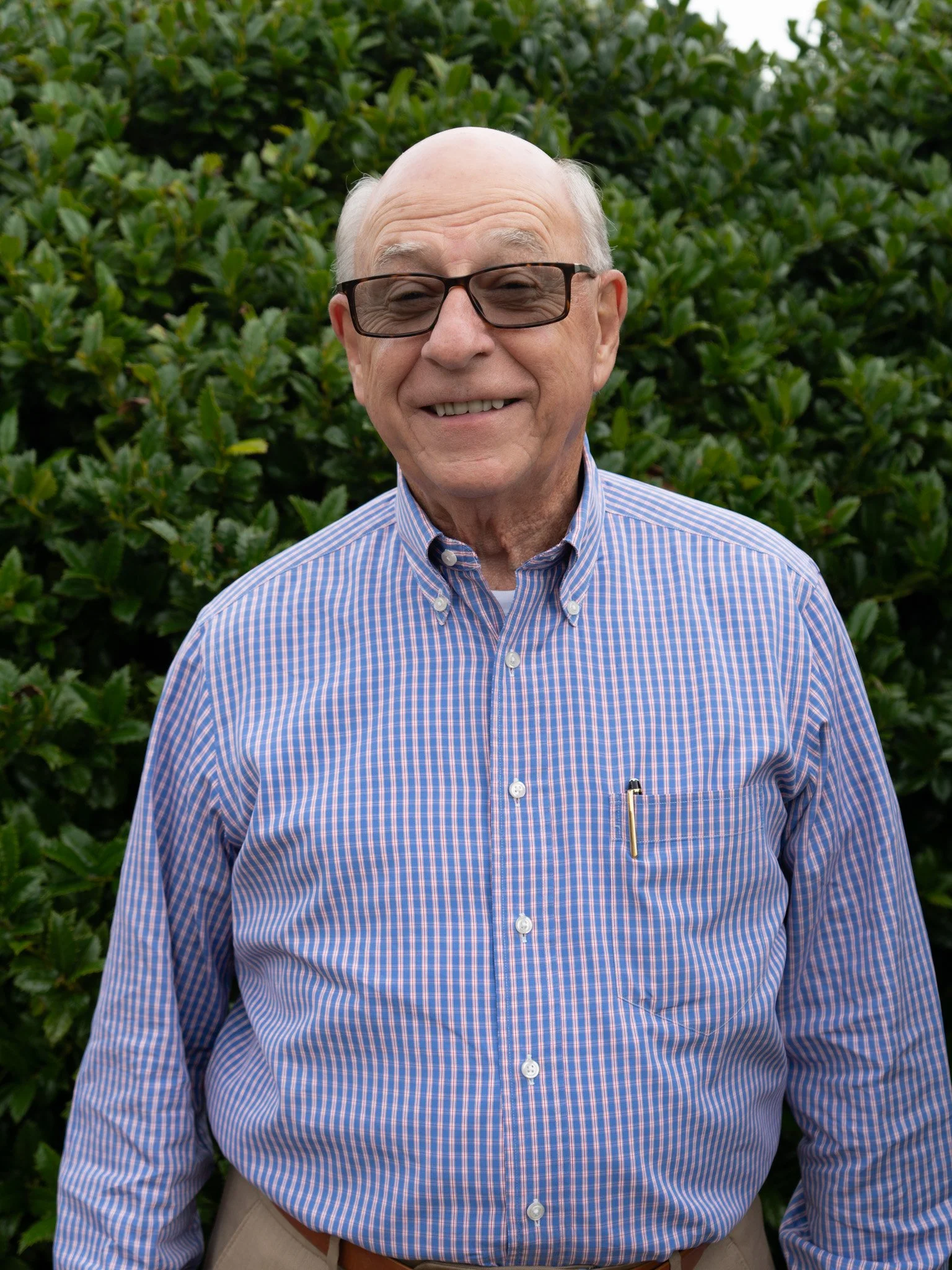 A smiling older man with glasses wearing a light green zip-up sweater stands indoors in front of decorative wall art.