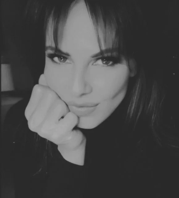 A black-and-white close-up photo of a woman with long hair, resting her face on her hand.