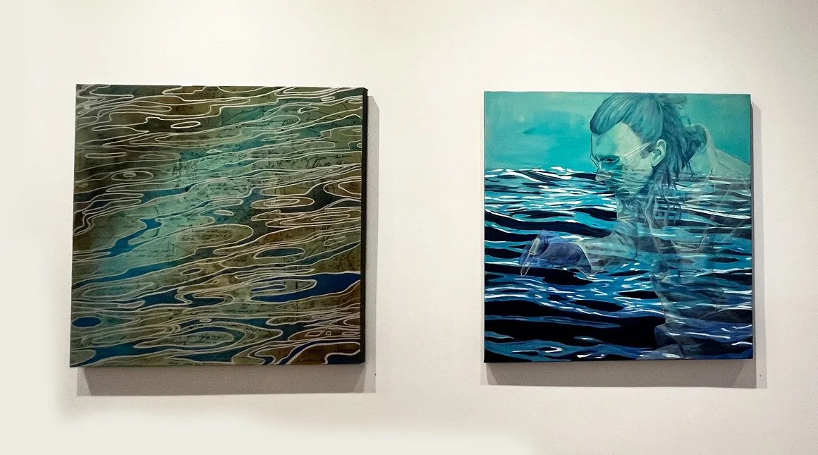Two paintings on a white wall. The left painting depicts a water surface with swirling patterns. The right painting shows a scientist doing ocean research, partially submerged in water, with reflections on the water's surface.