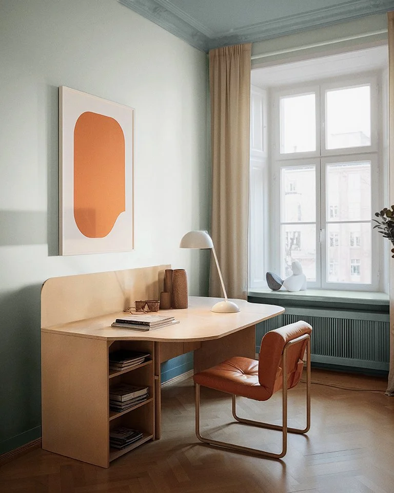 Flügger AI generated scene by Scenes. Minimalist home office with wooden desk, orange abstract art, leather chair, and large window with beige curtains.