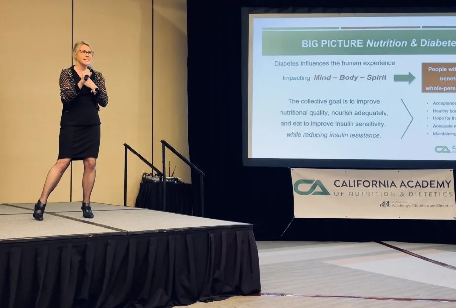 Person giving a presentation on nutrition and diabetes at a conference. A slide on the screen discusses the impact of diabetes on body, mind, and spirit, with a goal to improve nutritional quality and insulin sensitivity. A banner reads 'California A