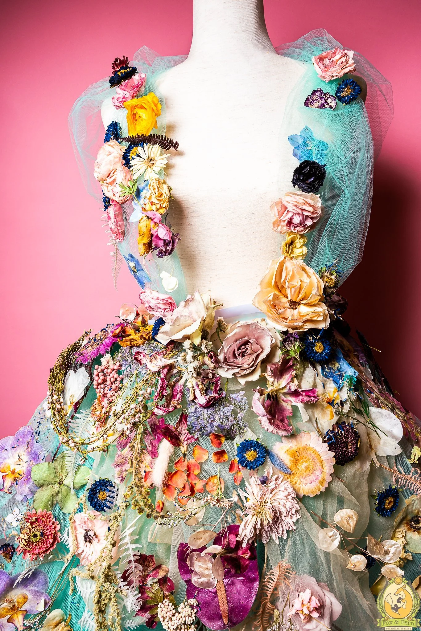 A dress decorated with colorful flowers and botanical elements against a pink background.