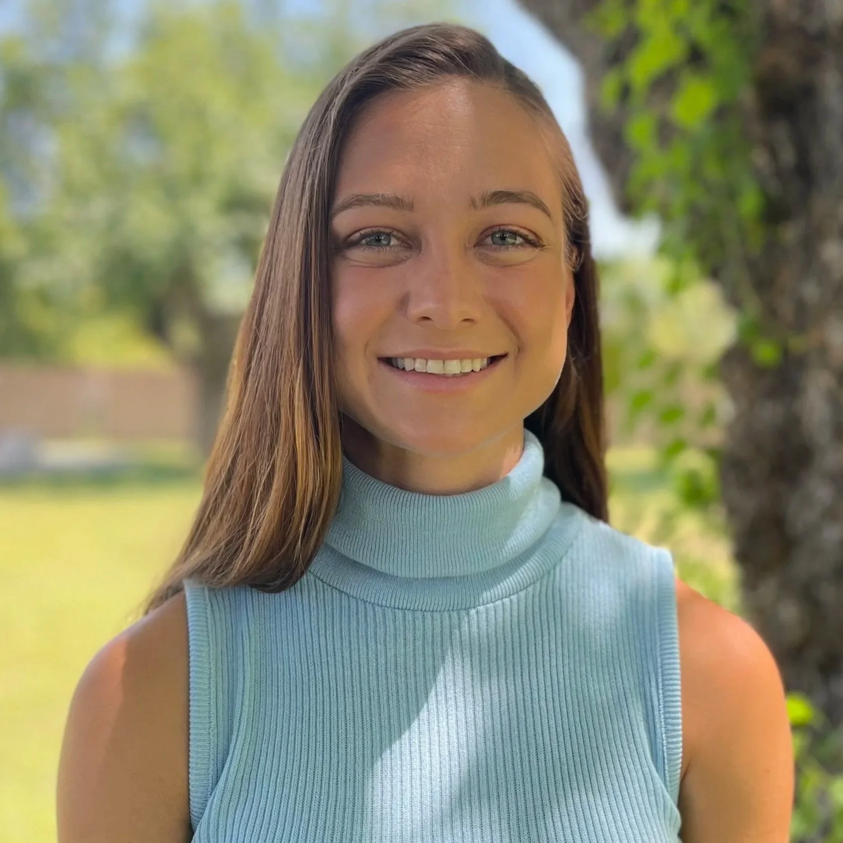 A close-up of a young woman smiling outdoors, wearing a light blue sleeveless top, with trees and greenery in the background. Madison Grayson, P.E. Civil Engineer
