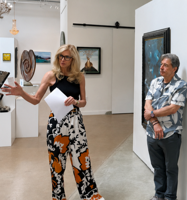 Two people in an art gallery conversing, with various paintings and sculptures on display in the background.