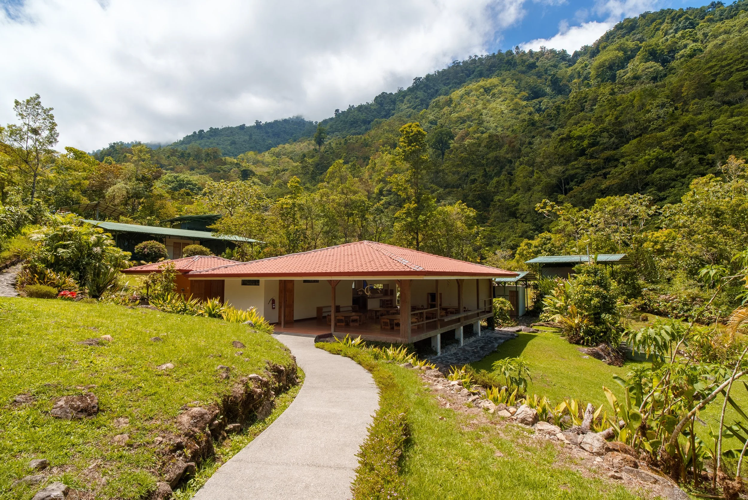 Casa de madera con techo rojo en medio de un paisaje montañoso con árboles y vegetación verde
