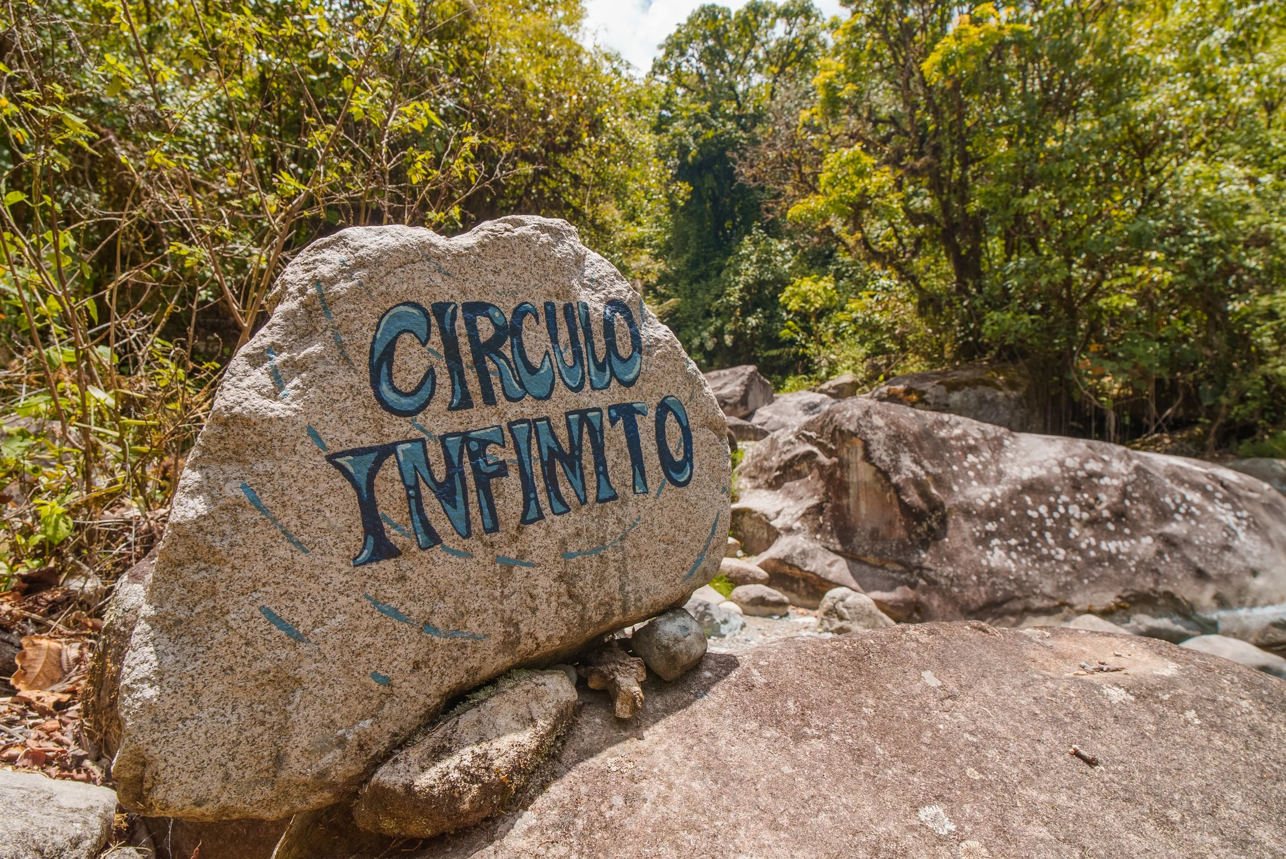 Roca con inscripción en pintura azul que dice 'Círculo Infinito', rodeada de vegetación y rocas en un entorno natural.