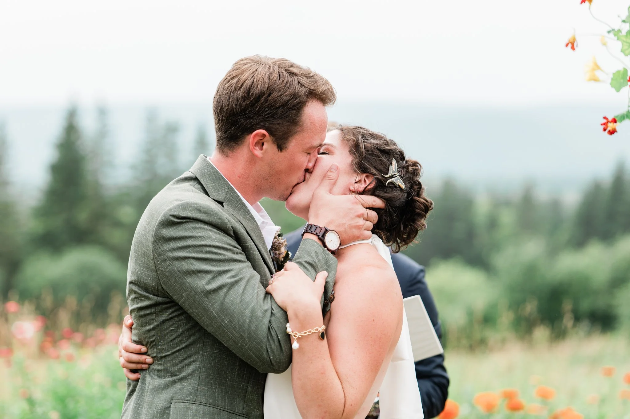 A couple sharing a kiss during their wedding outdoors with greenery and flowers in the background.