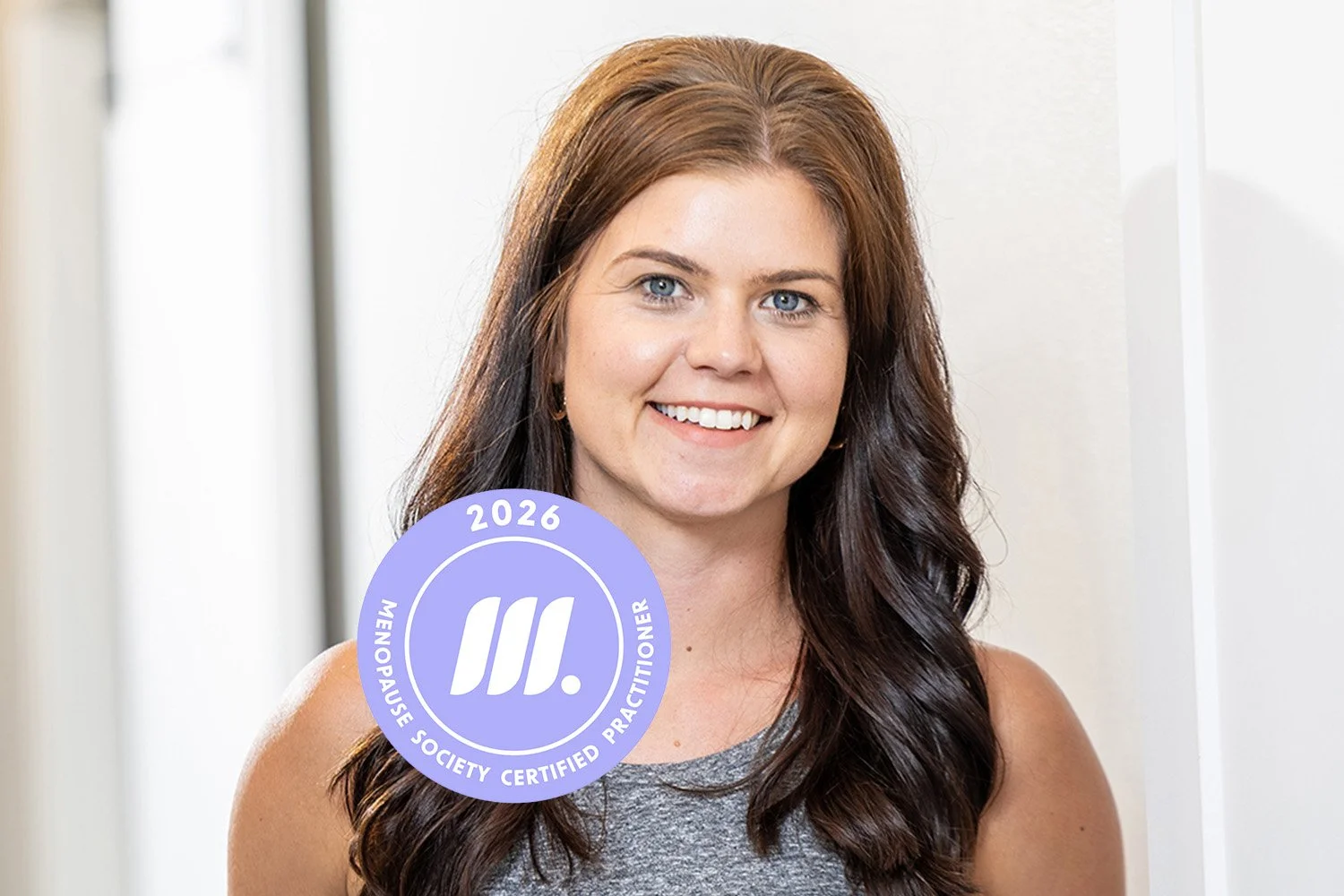 Women's health and obesity specialist, Stephanie Severson, with long brown hair, blue eyes, and light skin, smiling, wearing a sleeveless gray tank, standing indoors.