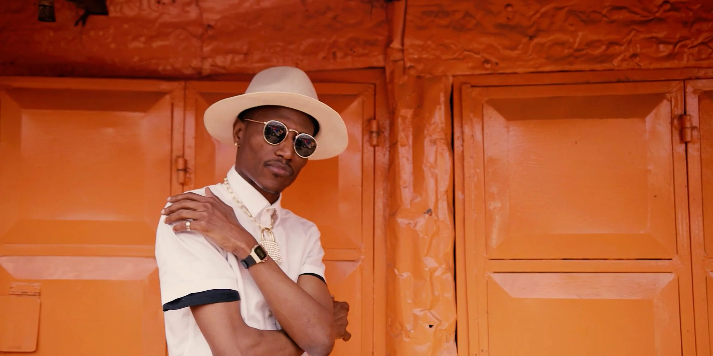 A male singer wearing sunglasses, striking a confident pose with his hands crossed