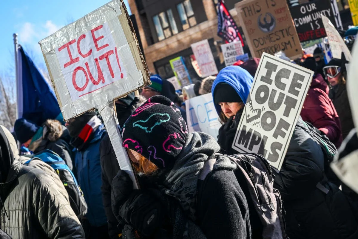 People at a protest holding signs, including one that says 'ICE OUT!'.